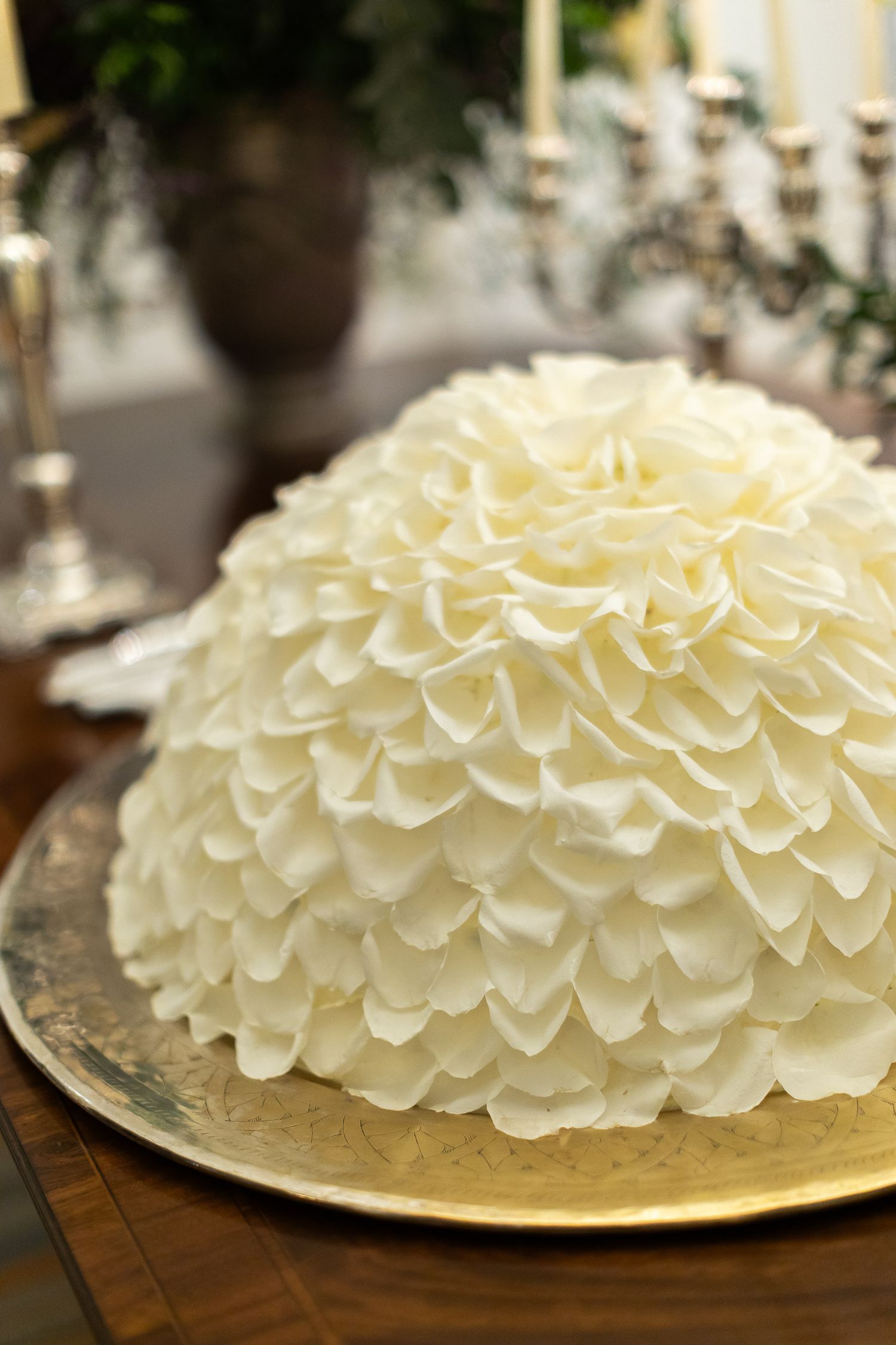 White frosted cake with delicate ruffled layers arranged in a beautiful floral pattern on a cream colored plate.