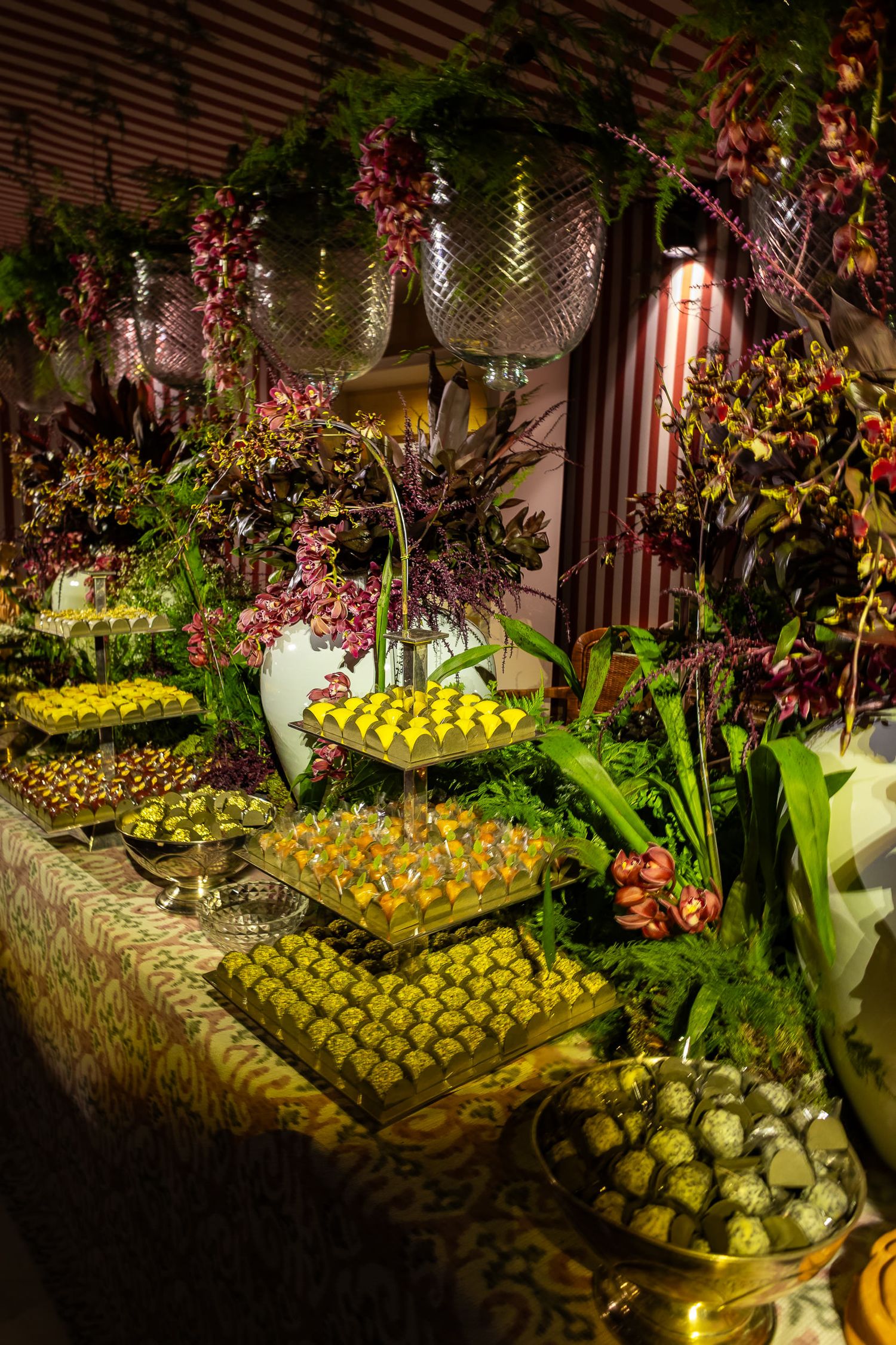 Elegant buffet display featuring rows of yellow desserts and tropical fruits arranged on tiered platters with floral decor.