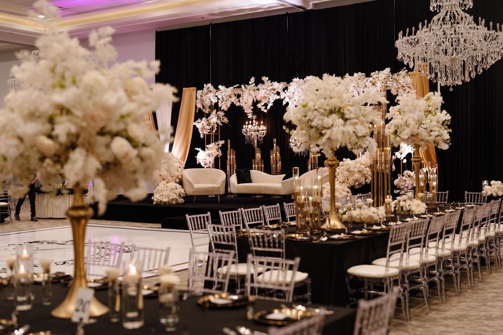 Elegant black and gold wedding reception with tall white floral centerpieces and crystal chandeliers.
