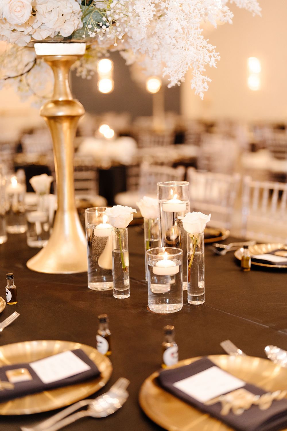 Luxury wedding table setting with gold charger plates, floating candles, and tall white floral centerpieces.