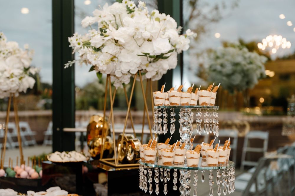 Elegant wedding dessert display with crystal stand, mini desserts, and tall white floral arrangement.