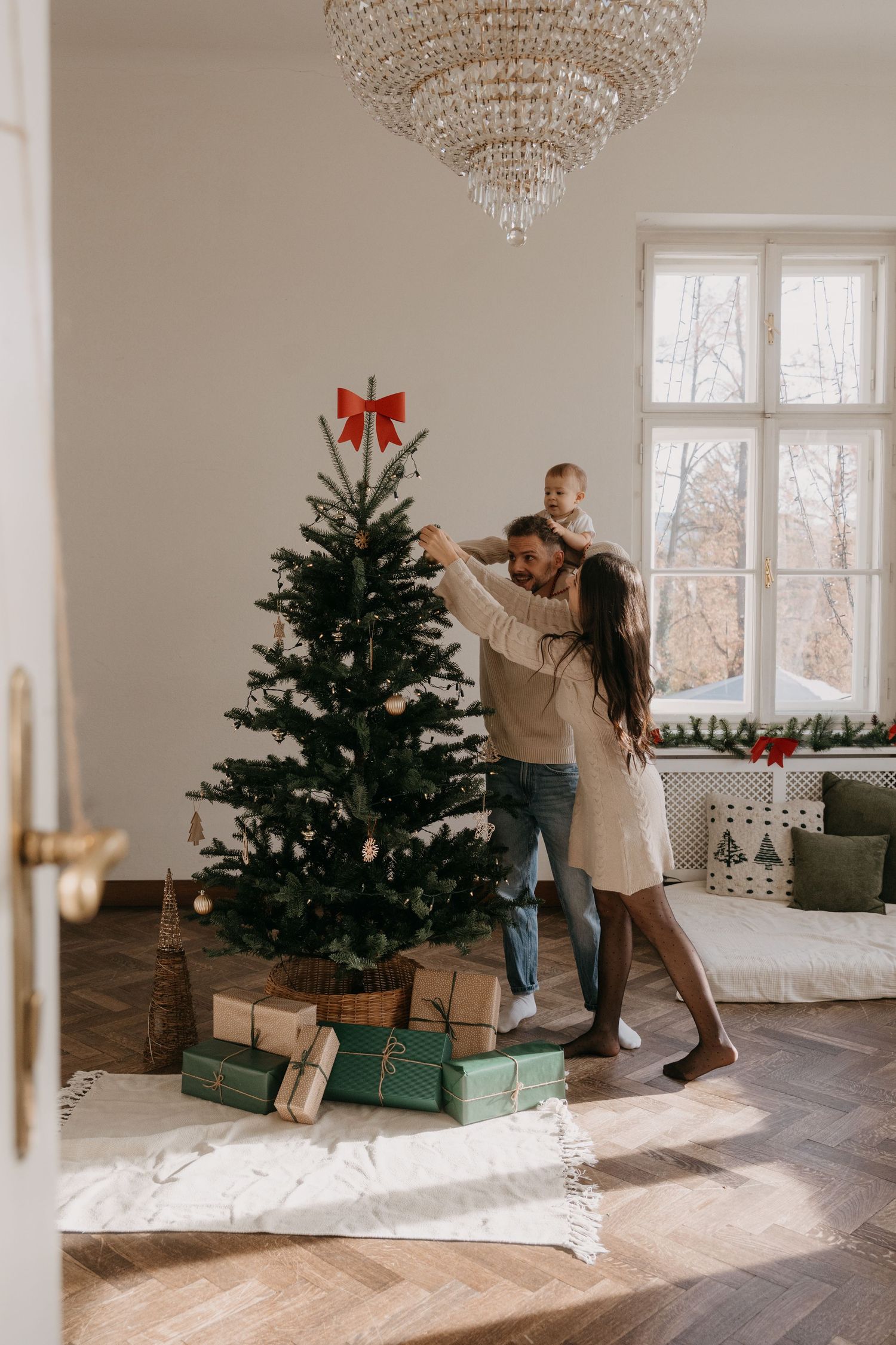 Sequence of photos showing a Christmas tree being set up in an elegant room with herringbone floors and crystal chandelier.