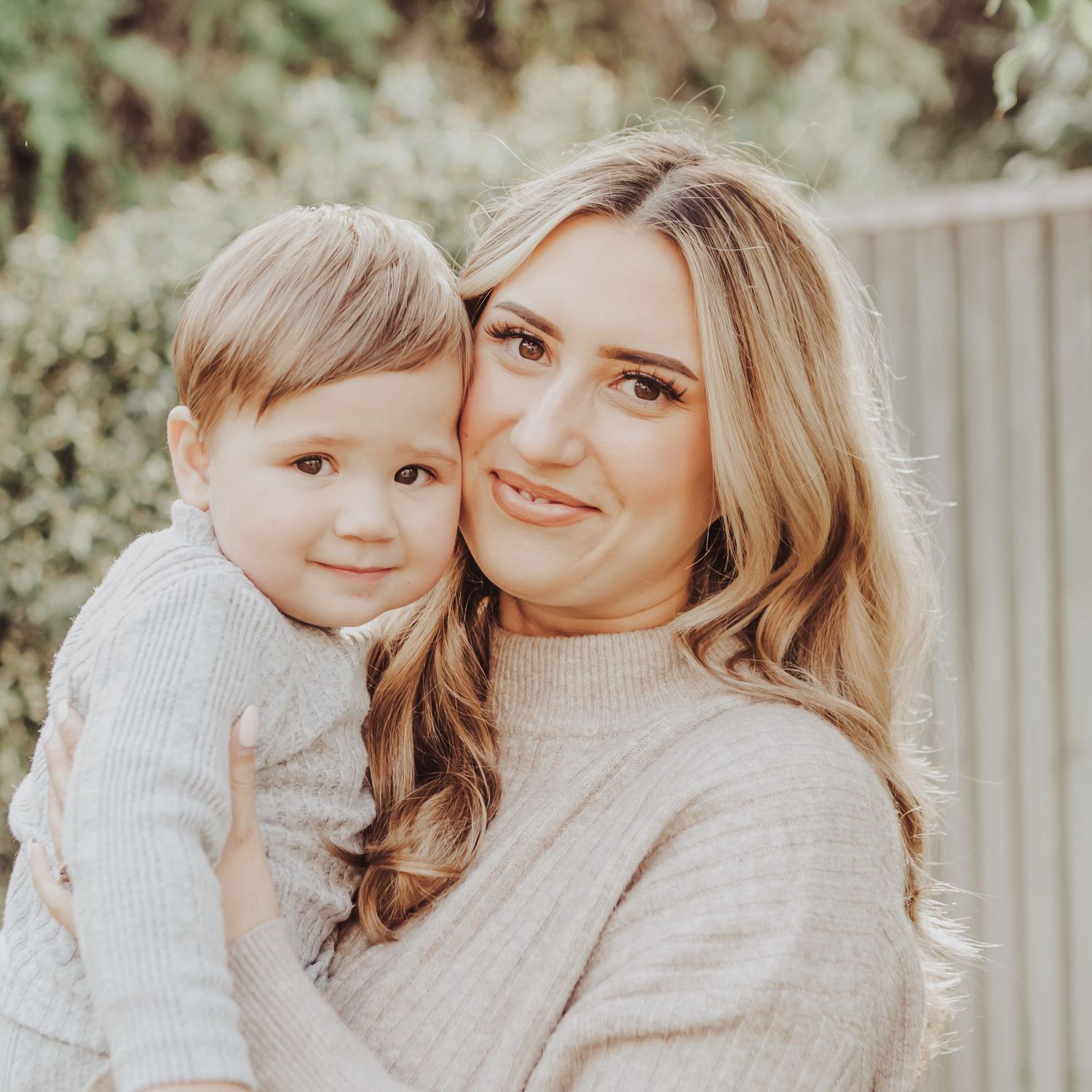 Cosy cuddle with a little boy and his mum smiling at the camera.