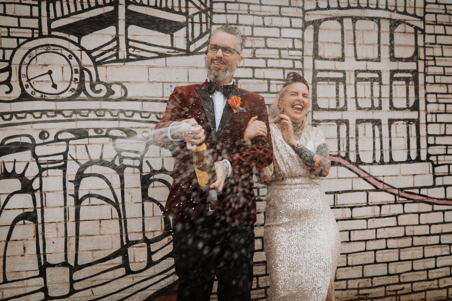 Bride and groom share a joyful moment while being showered with confetti outside a brick building.