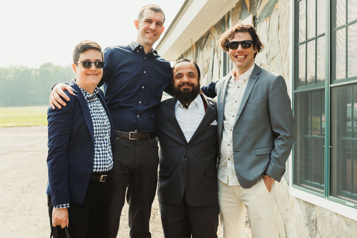 Group gathering outdoors in formal attire near a building with large windows.