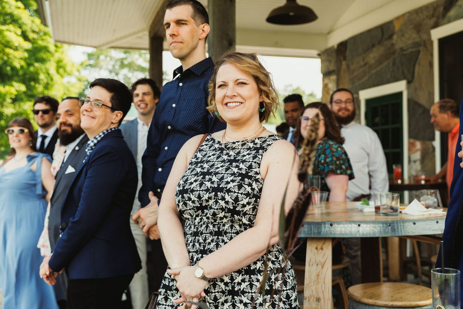 Casual outdoor celebration with guests gathered on a porch near greenery.