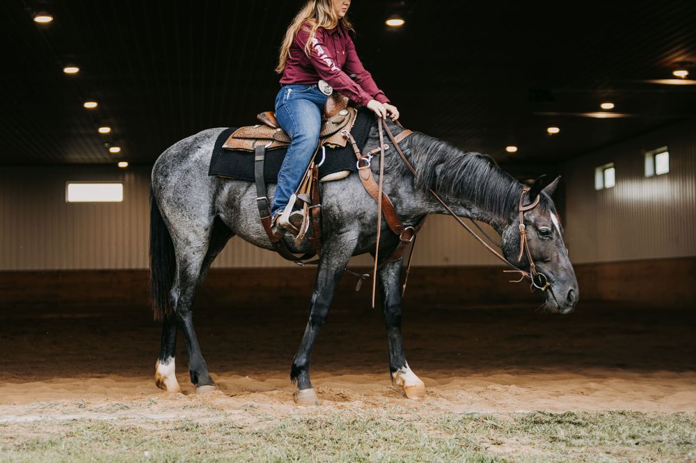 Riders practice horseback riding techniques in an indoor arena with sandy footing.