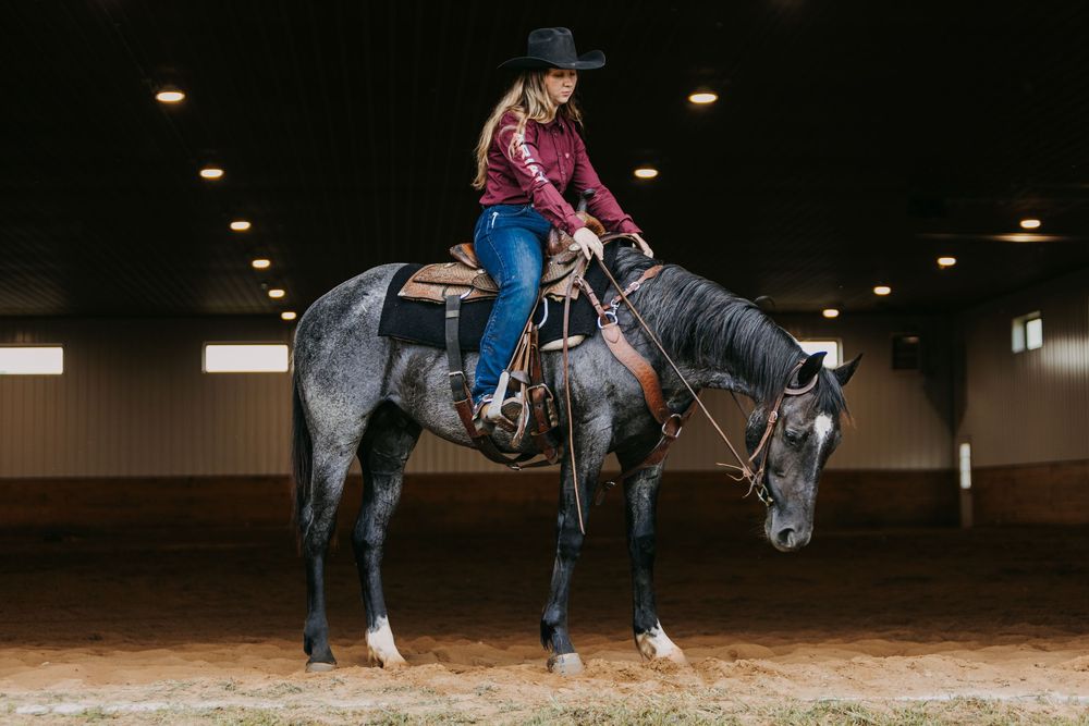 Riders practice horseback riding techniques in a dimly lit indoor arena during an equestrian training session.