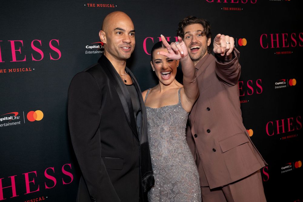 Group of people pose together at red carpet event for Chess musical premiere with Mastercard branding visible in background.