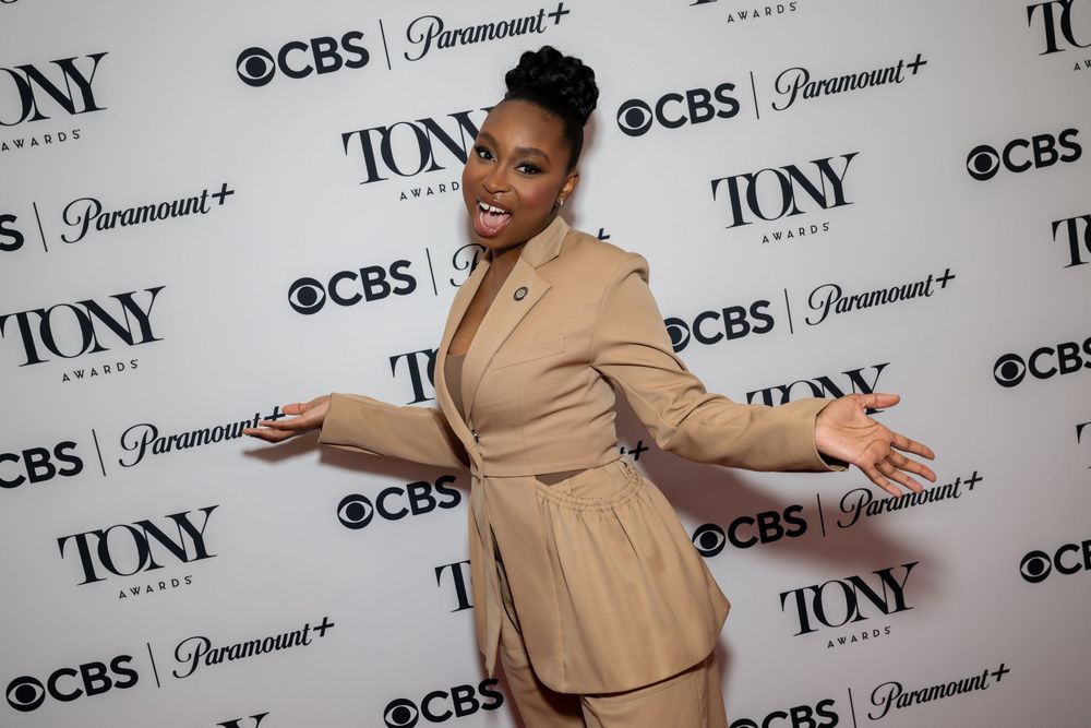 Woman in beige suit posing at Tony Awards CBS Paramount+ red carpet event with arms outstretched.