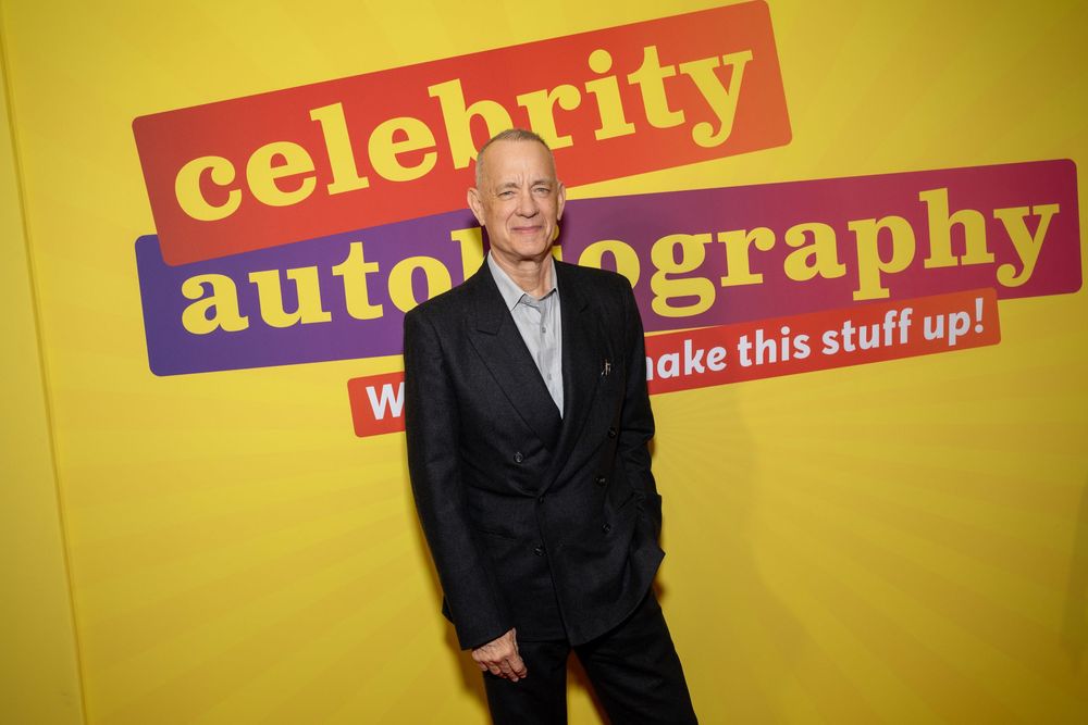 Man in black suit posing at Celebrity Autobiography yellow event backdrop.