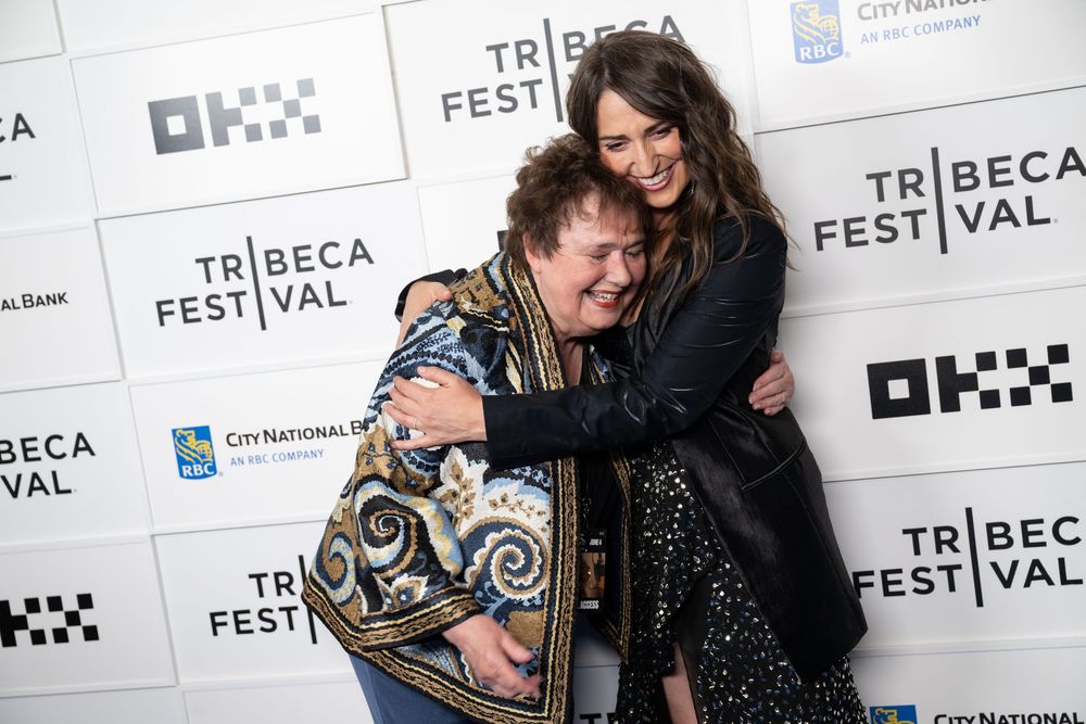 Two women share a warm hug on the Tribeca Festival red carpet event backdrop.