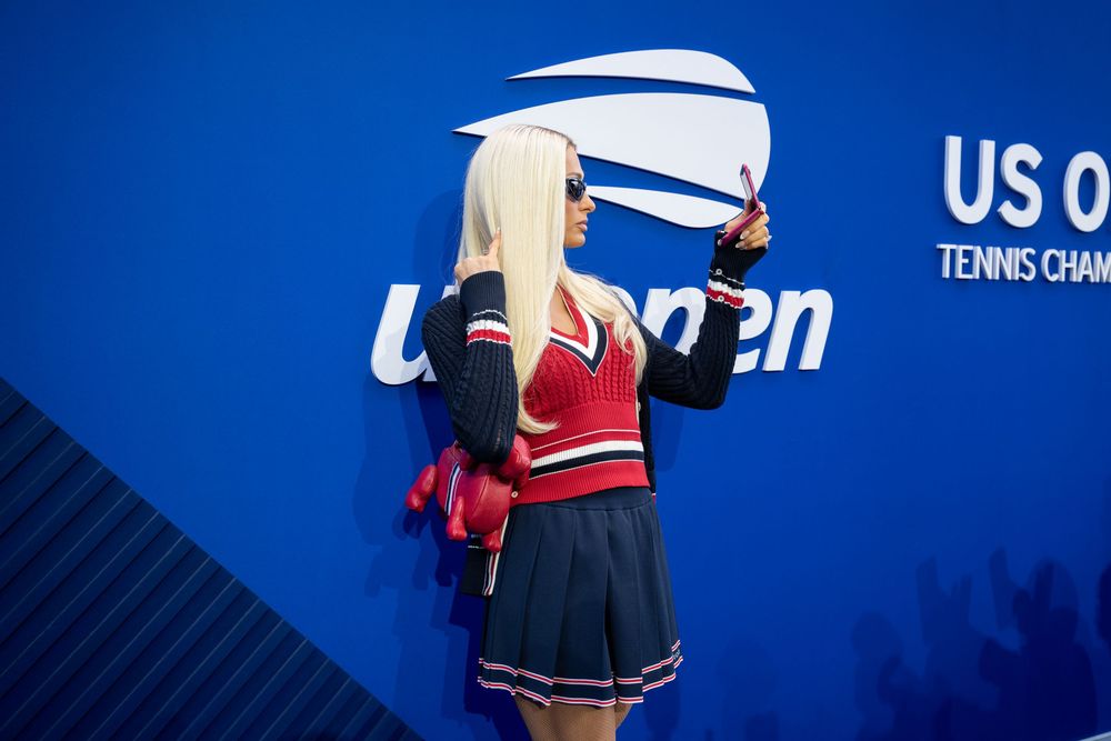 Cheerleader in red and navy outfit poses at US Open Tennis Championships blue wall backdrop.
