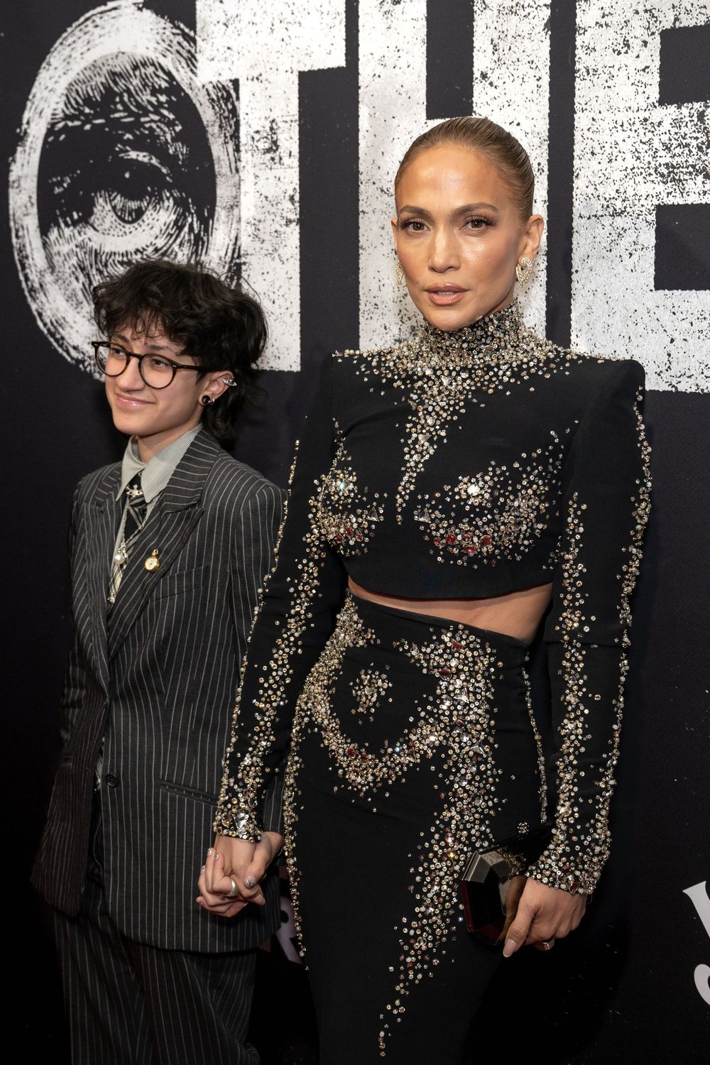 Two people pose together at a formal event wearing contrasting pinstripe and sparkly black outfits.