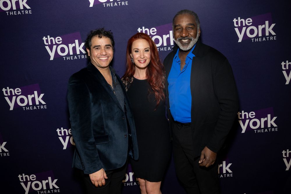 Three people smiling together at The York Theatre event, posing in front of a purple branded backdrop.