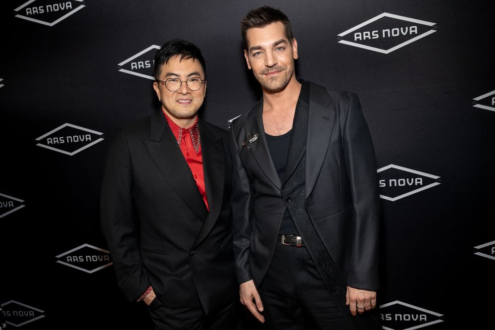 Performers pose together at an entertainment industry event with black and red outfits against a dark backdrop.