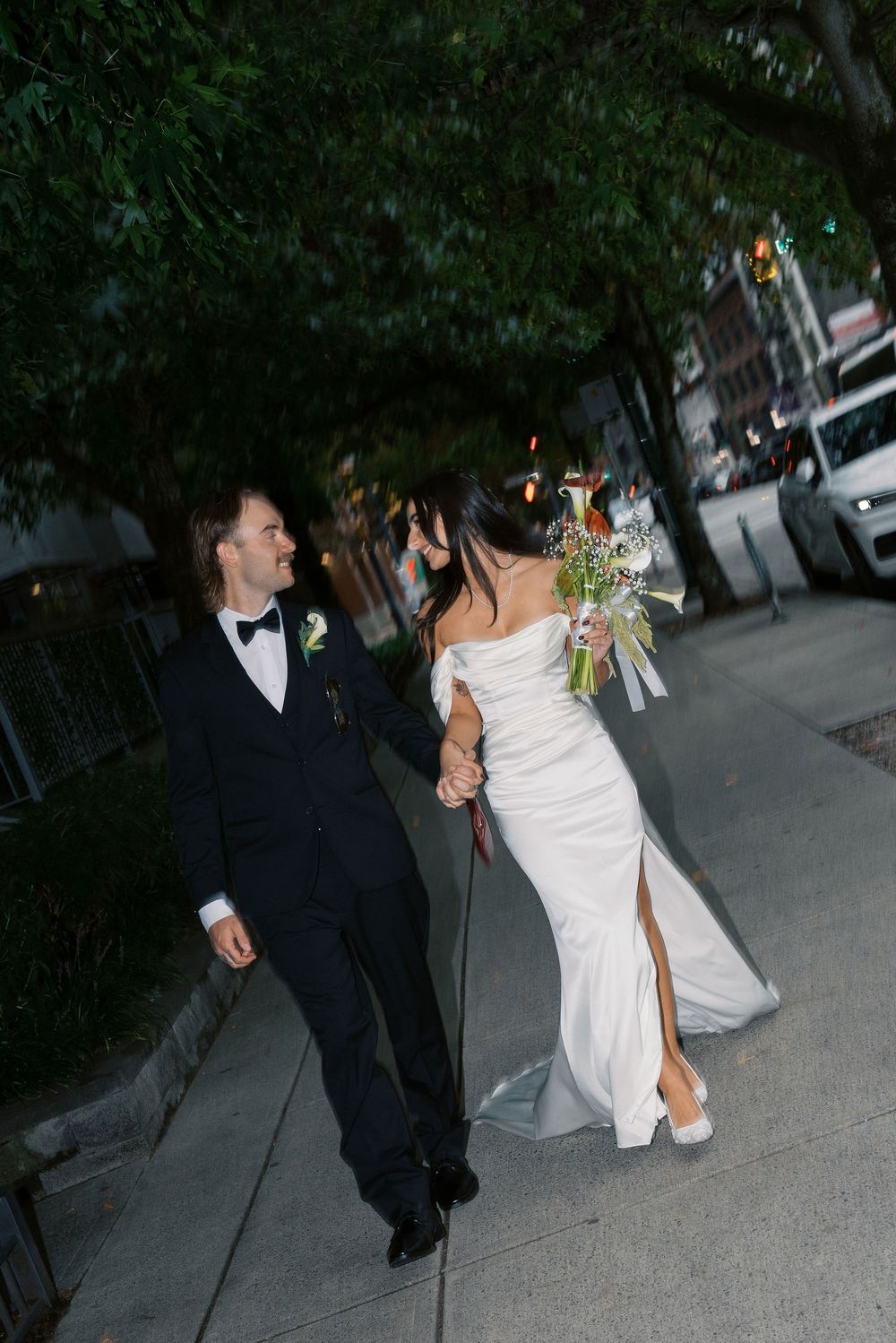 A couple shares a playful moment on a city street after their wedding celebration.