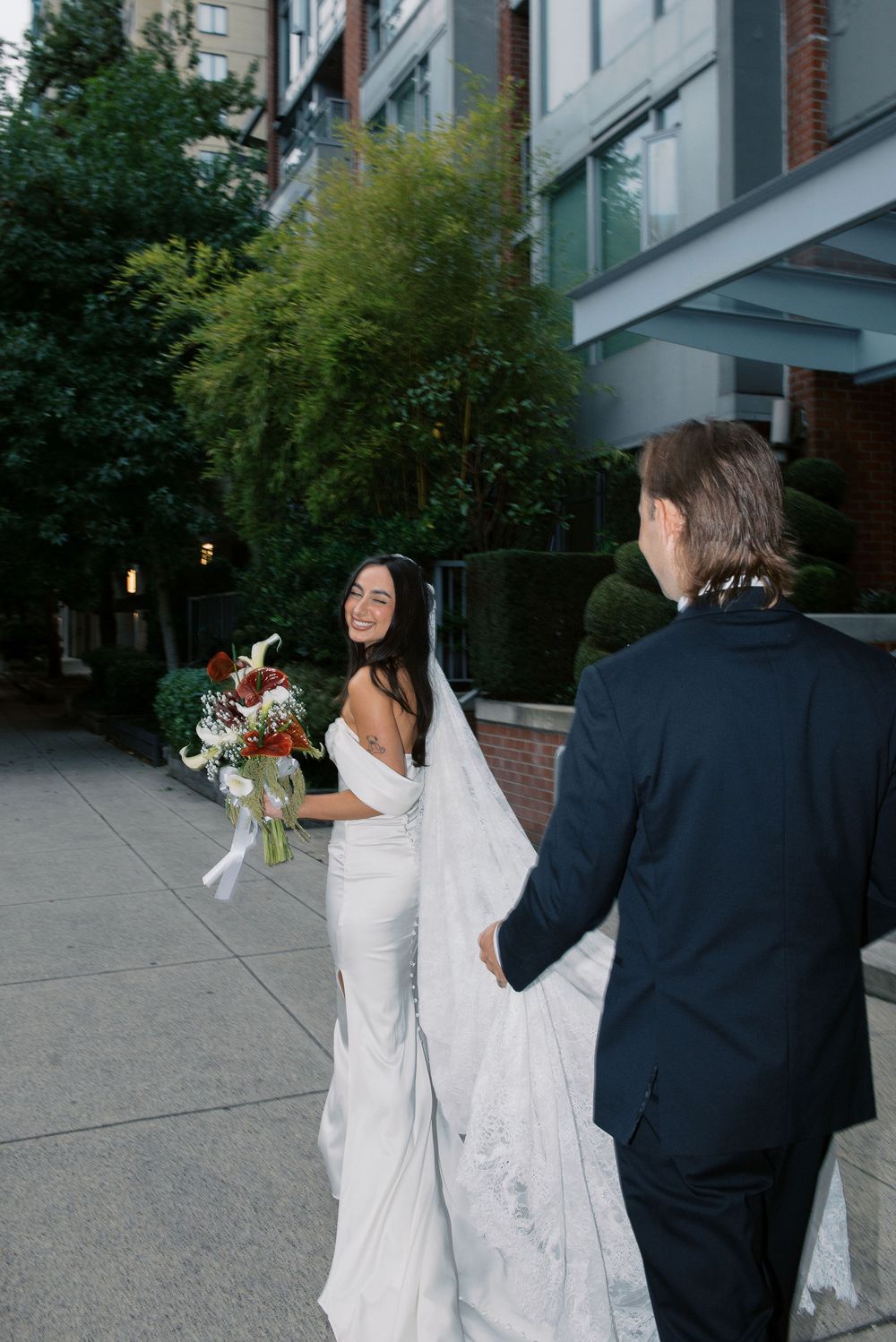 A sequence of photos showing a couple in wedding attire playfully dancing and twirling together on a city sidewalk.