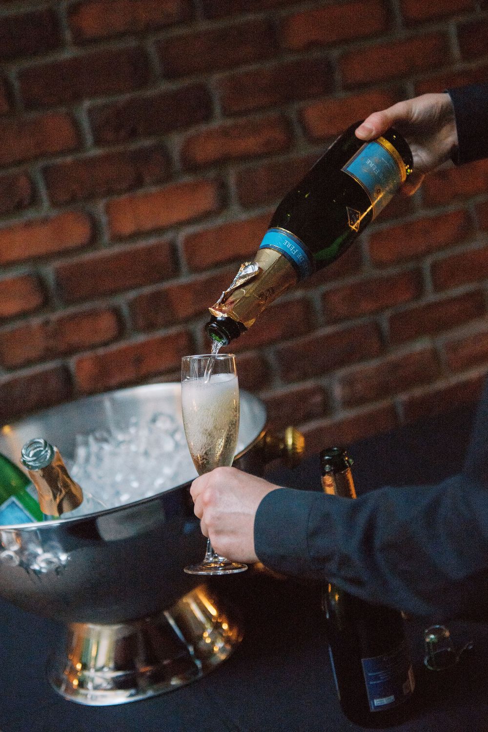 Champagne being poured into a glass against a rustic brick wall background, showing multiple pouring stages.