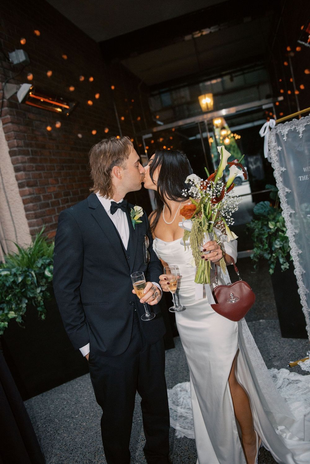 A couple shares a romantic moment at their wedding reception with twinkling lights and brick walls in the background.