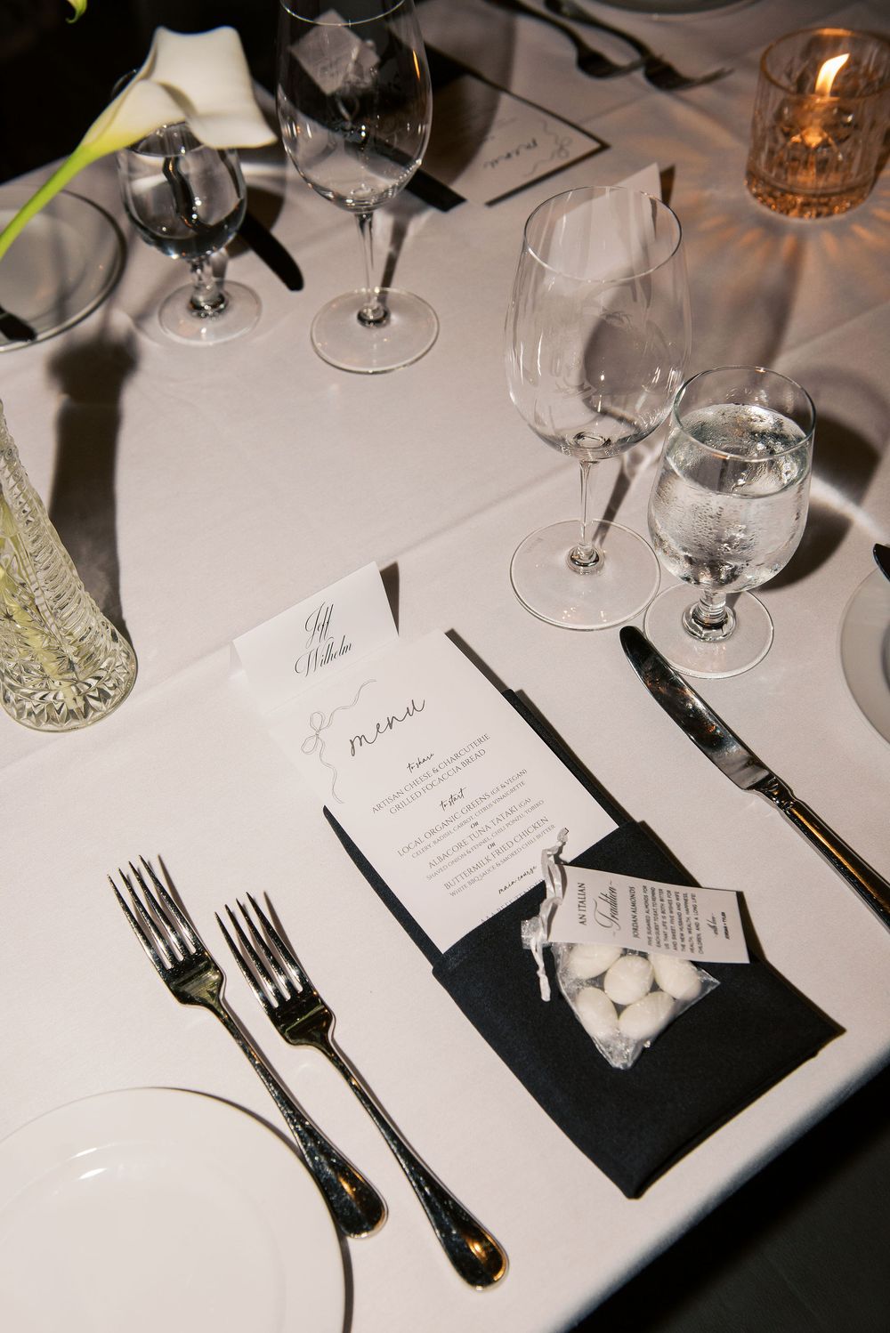Elegant table setting at upscale restaurant with wine glasses, silverware, menu and candlelight on white tablecloth.