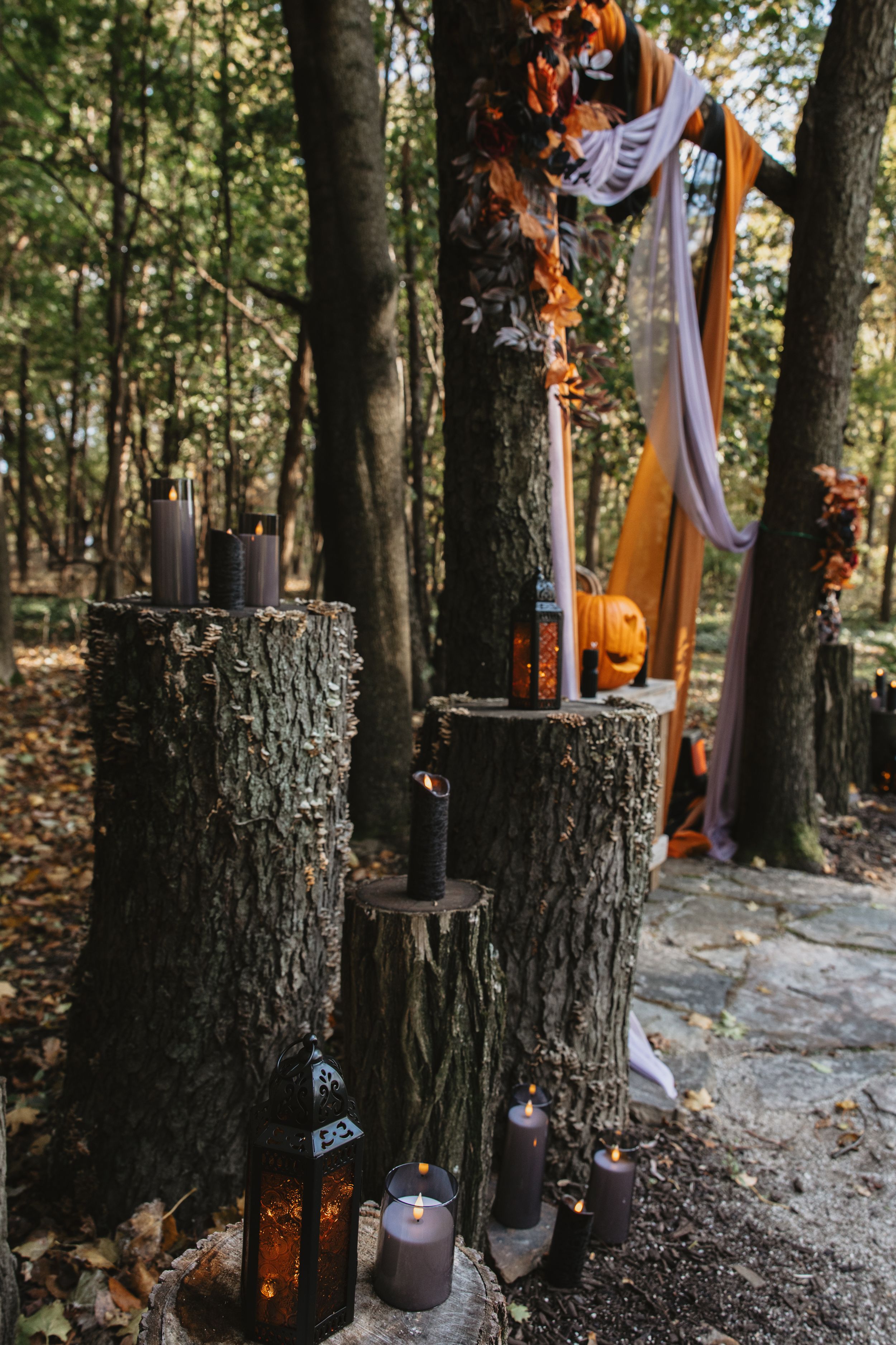 String lights and Halloween decorations illuminate a wooded path with carved pumpkins and spooky autumn ambiance.