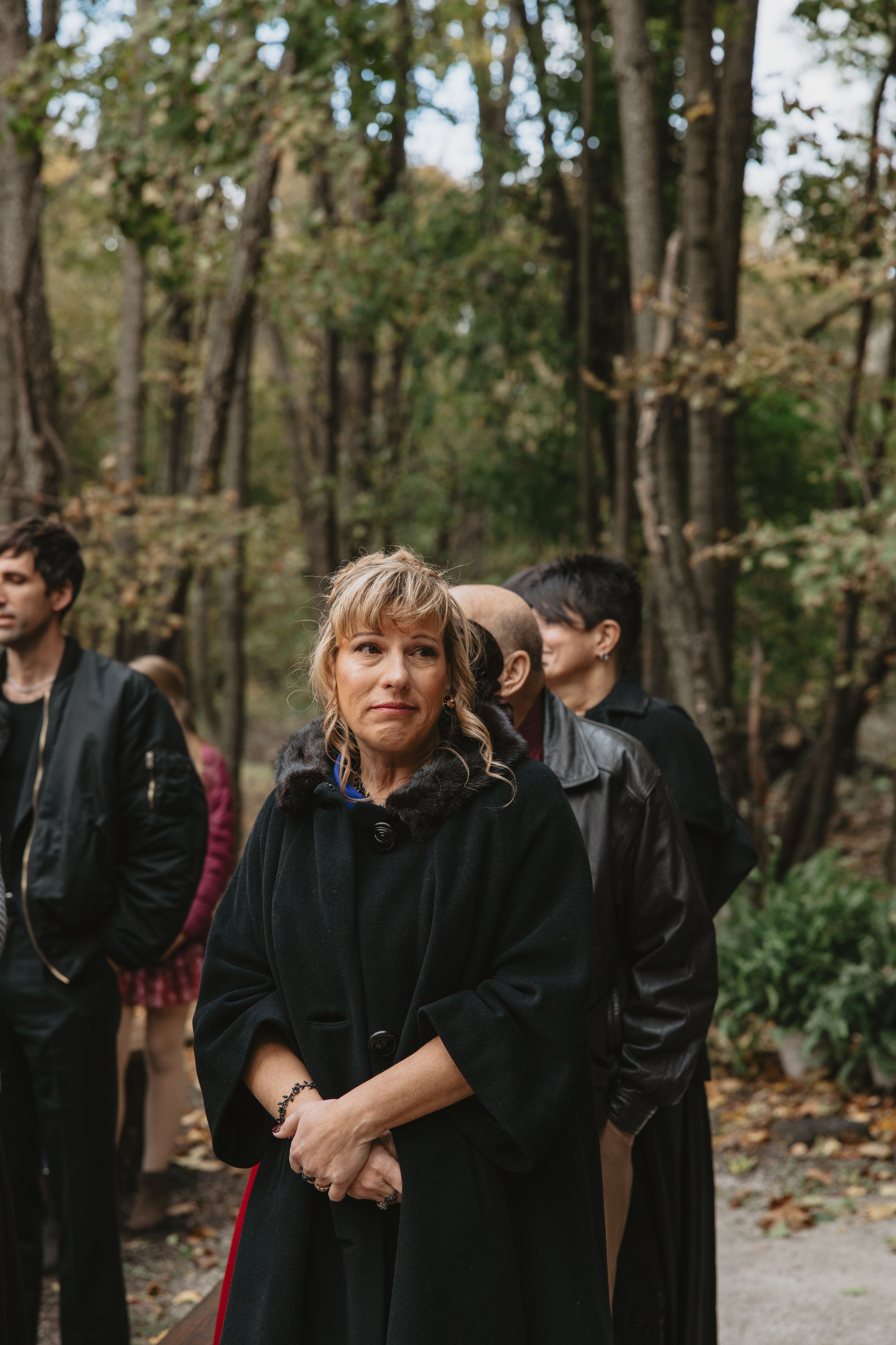A group gathers in a wooded area wearing dark clothing for what appears to be an outdoor autumn event.