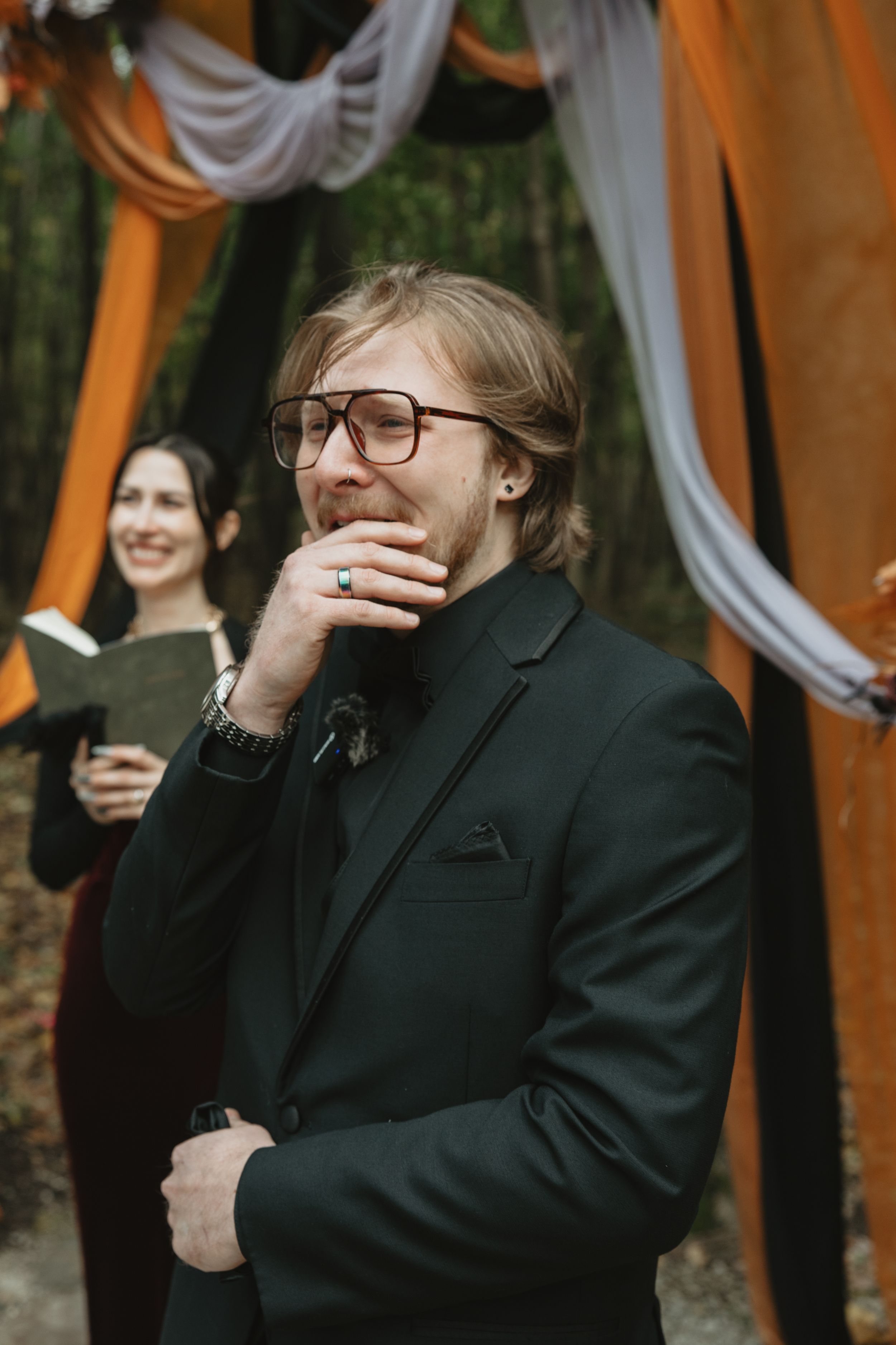 A sequence of candid emotional reactions showing someone in a black suit jacket and glasses against an orange backdrop.