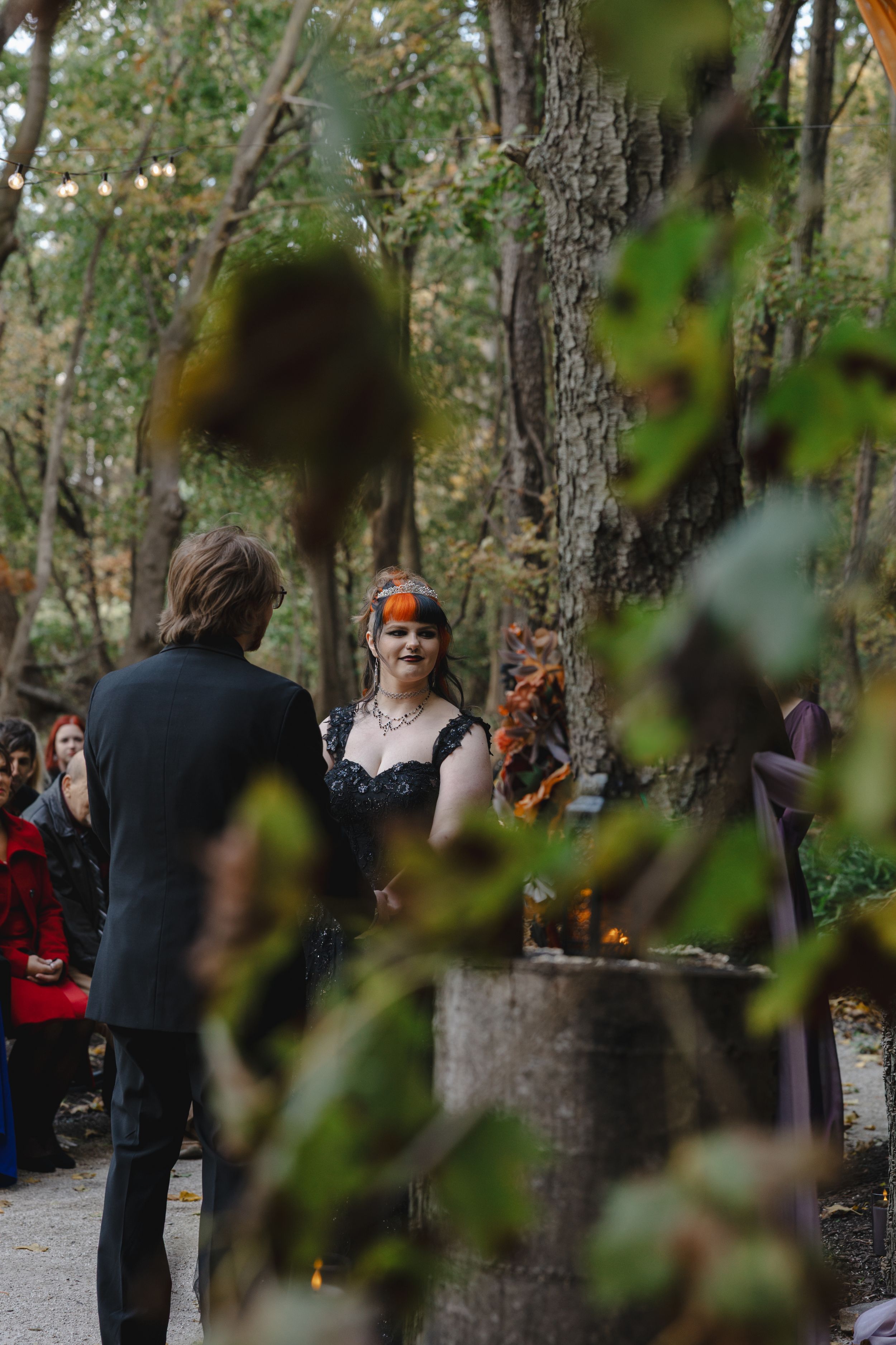 A group of people gather in a wooded area during what appears to be an outdoor event or ceremony.