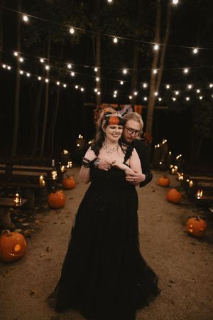 String lights create a romantic atmosphere over a dirt path decorated with pumpkins for an outdoor Halloween celebration.
