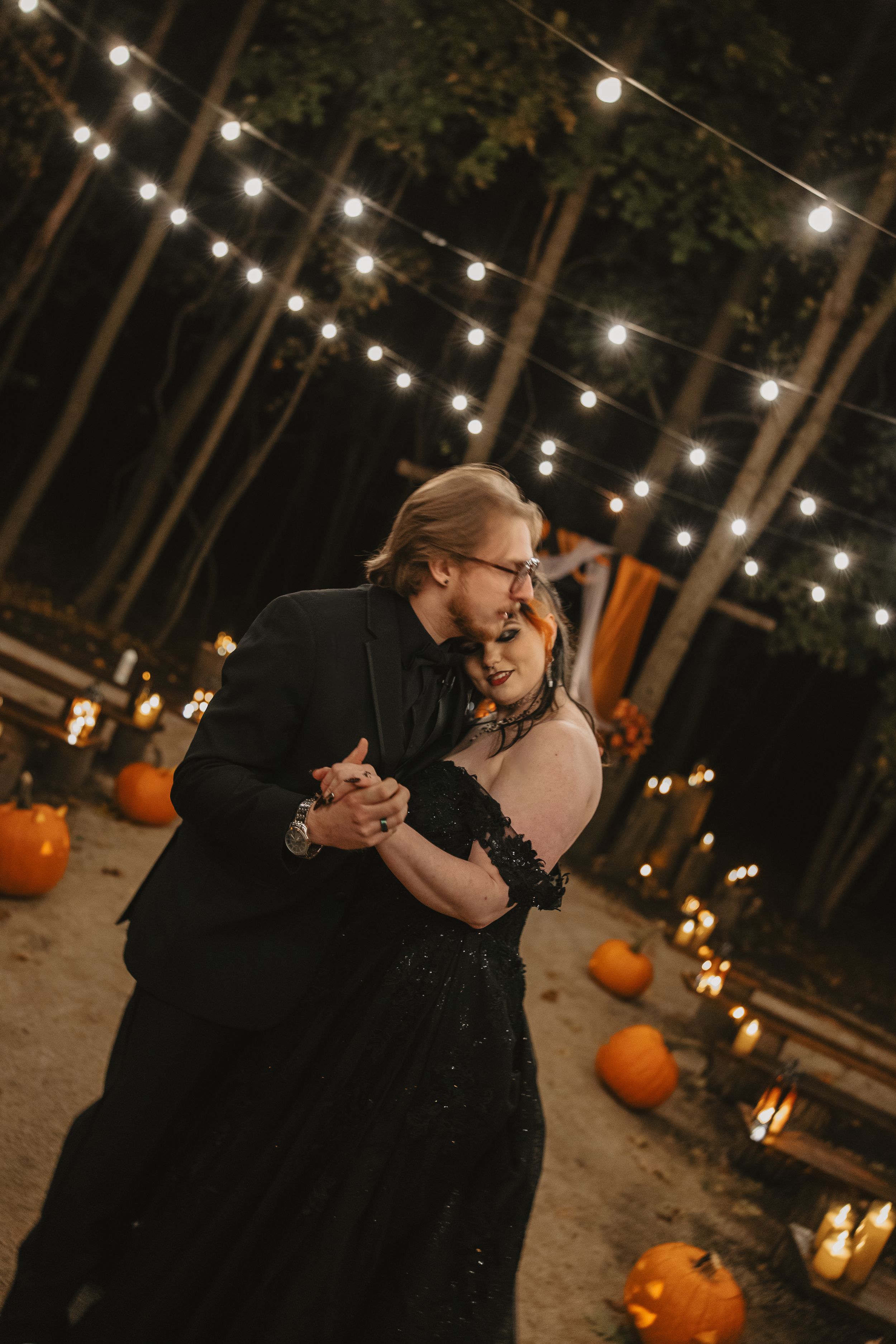 A couple dances under string lights with pumpkins and fall decor creating a romantic autumn atmosphere.