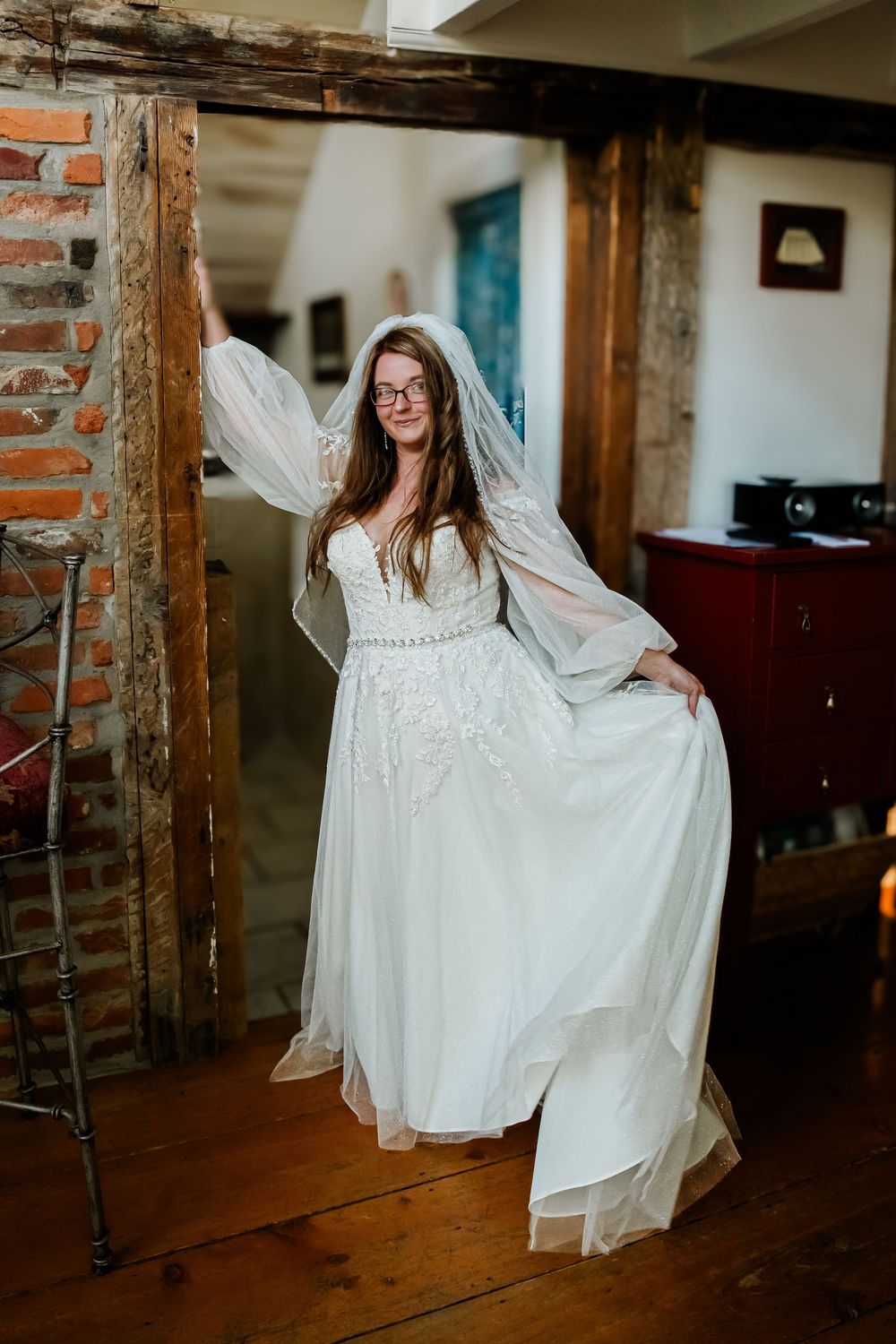 Woman in flowing white dress twirling in rustic indoor setting with exposed brick walls.