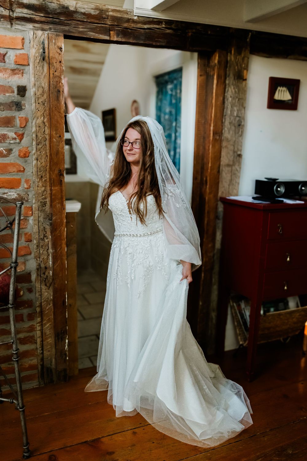 Bride in vintage-style white dress poses playfully in rustic indoor venue.
