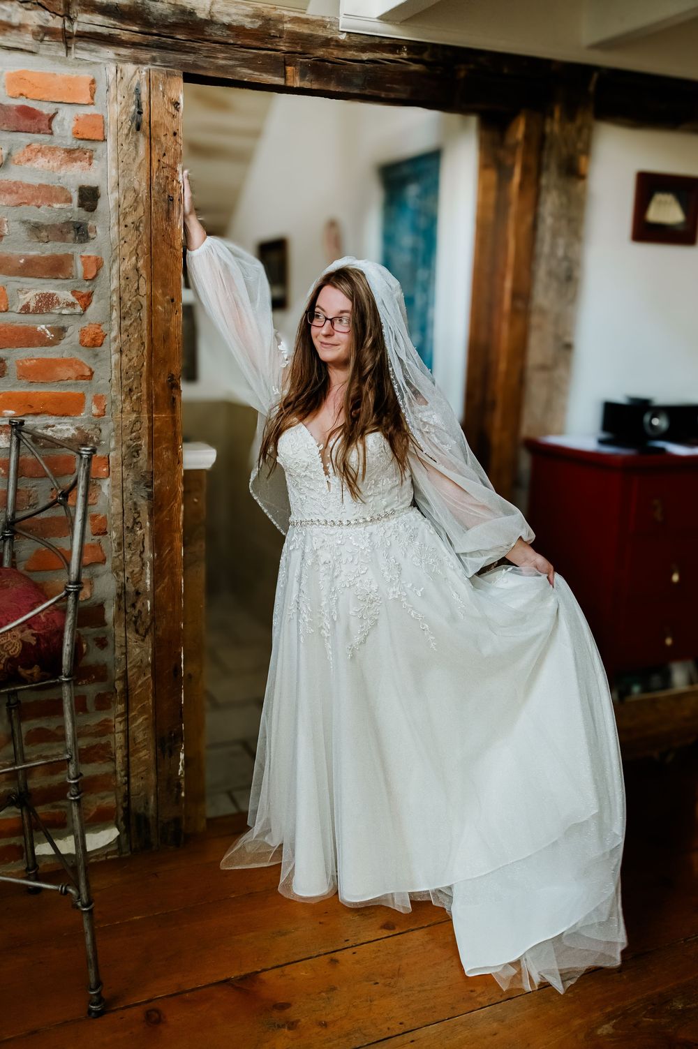 A flowing white wedding dress is showcased against a rustic brick wall backdrop.
