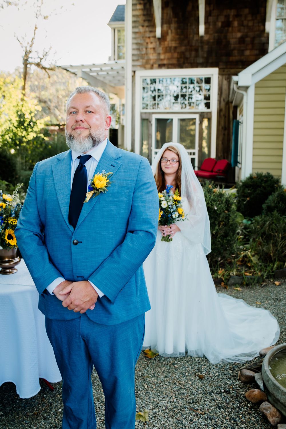 A wedding couple poses outdoors with yellow house and brick details in background.
