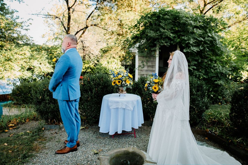 Garden wedding scene with blue-suited figure and billowing white bridal gown against natural foliage.