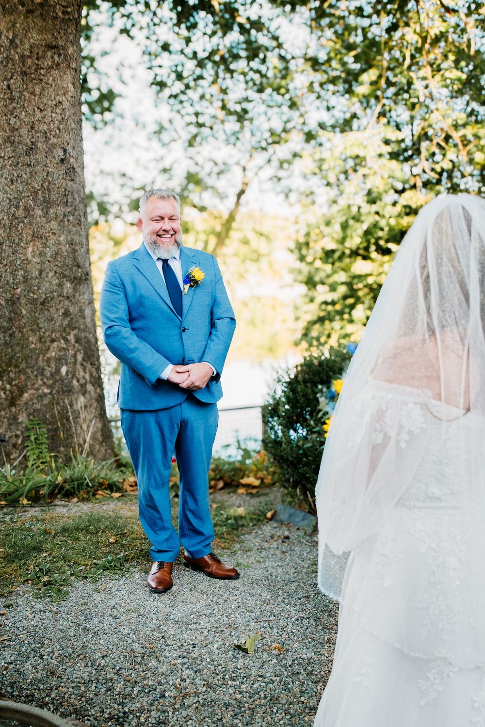 Outdoor wedding first look with bright blue suit and flowing white wedding dress among autumn trees.