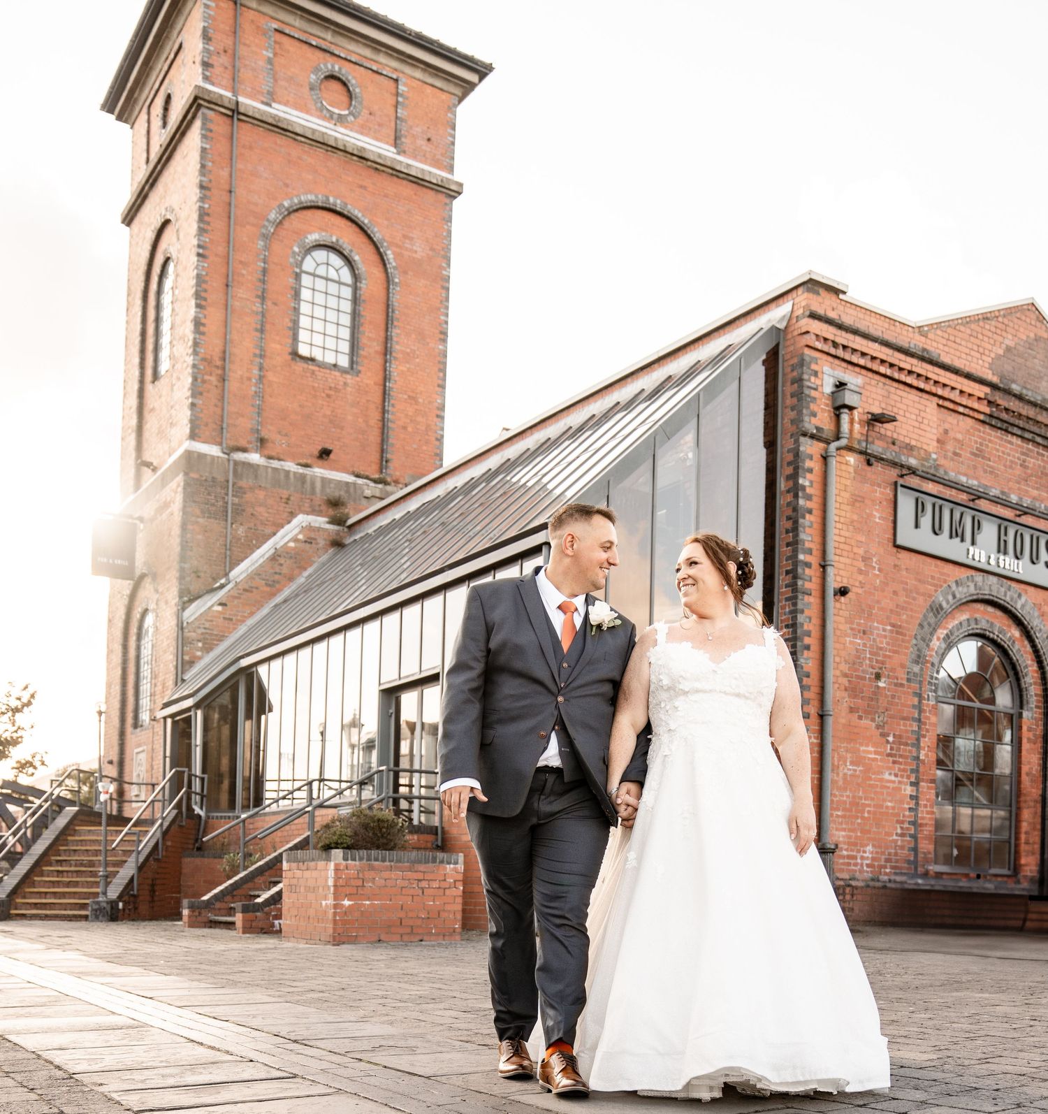 A couple shares romantic moments at a historic brick building venue with arched windows and industrial architecture.
