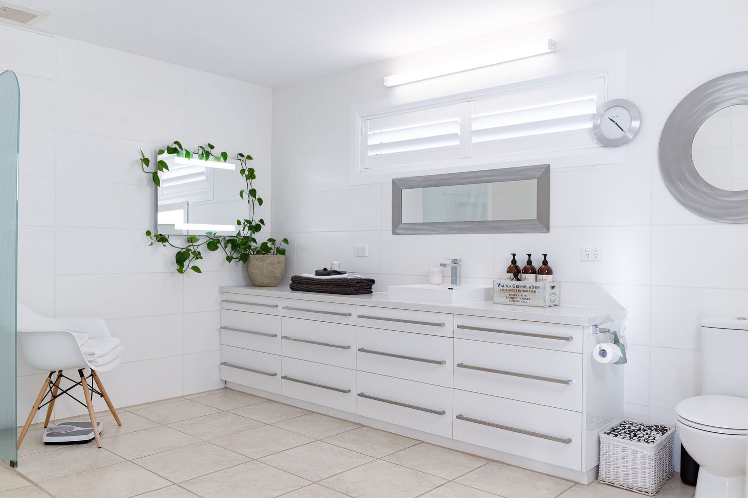 Modern minimalist white bathroom interior with sleek fixtures and built-in storage cabinets along the wall.