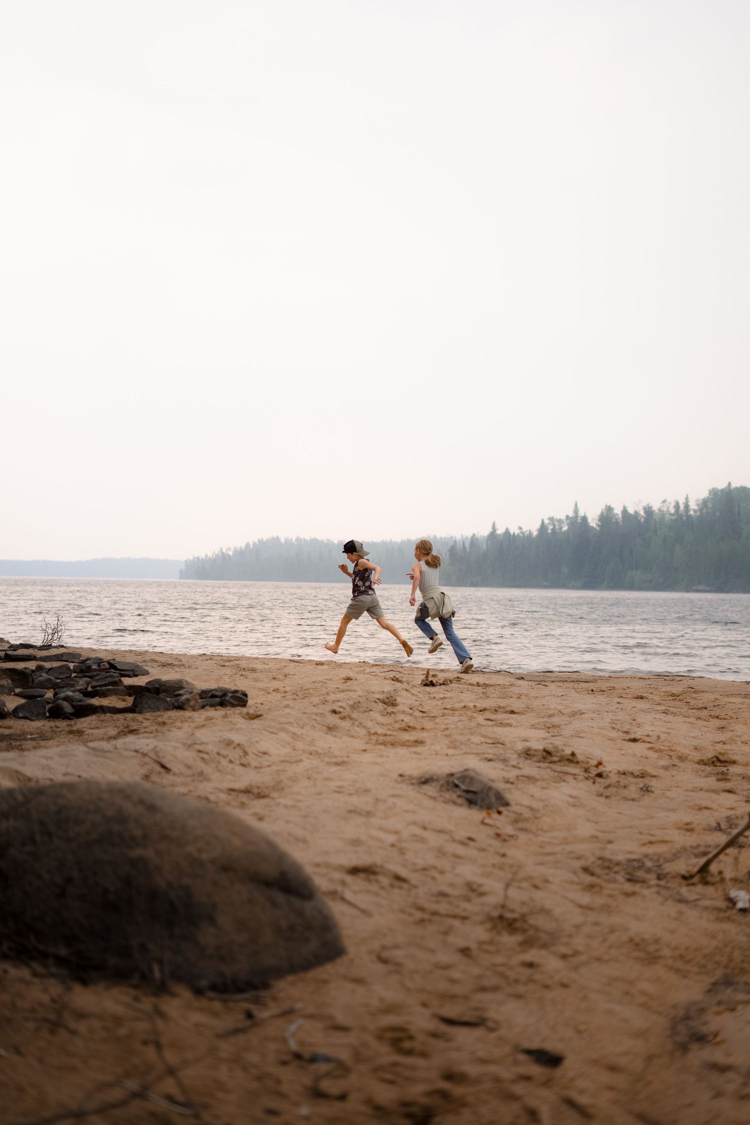 Sandy beach shoreline with distant forest and lake views during golden hour.