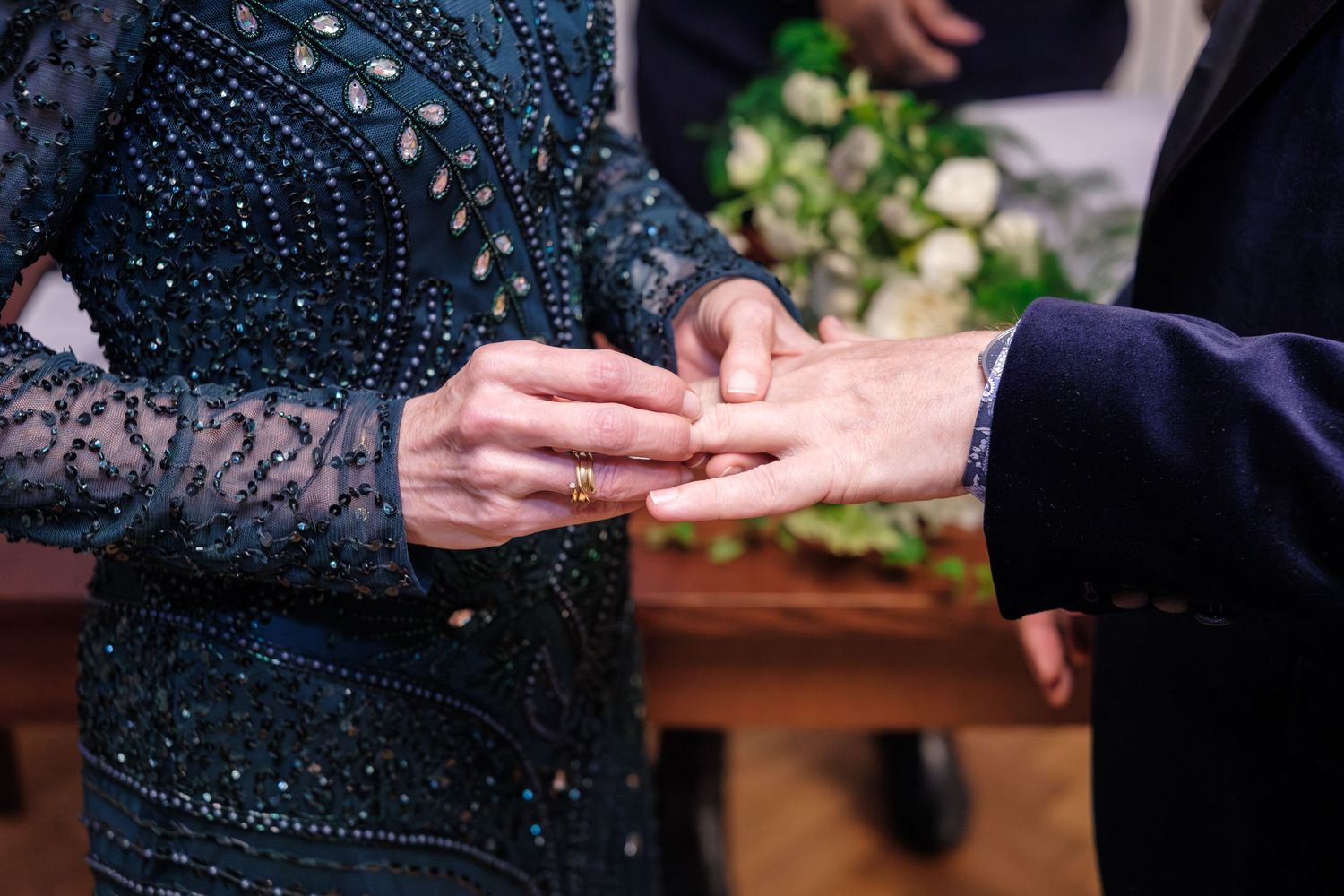 Close-up of hands exchanging rings during a wedding ceremony on a wooden surface.