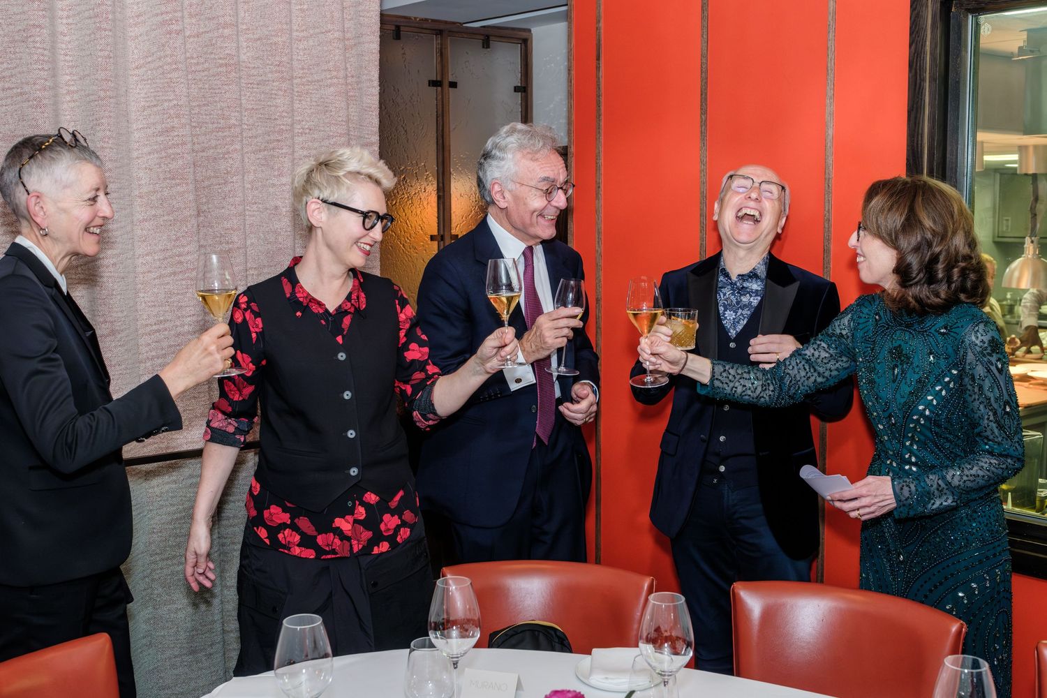 A group of seniors enjoying a social gathering at a restaurant with red walls and wine glasses on the tables.