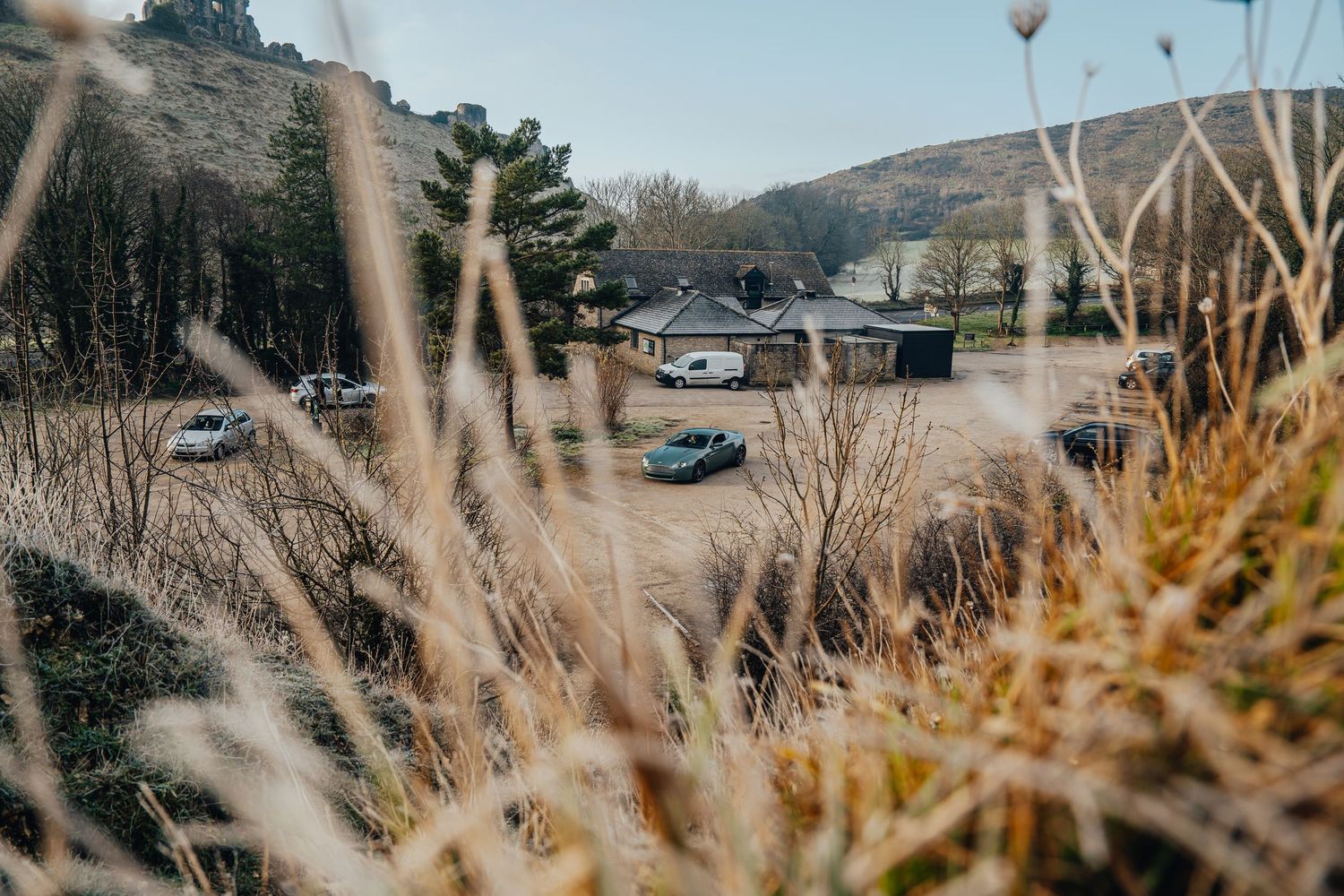Cars drive down a winding mountain road with scenic views through golden grass and trees.