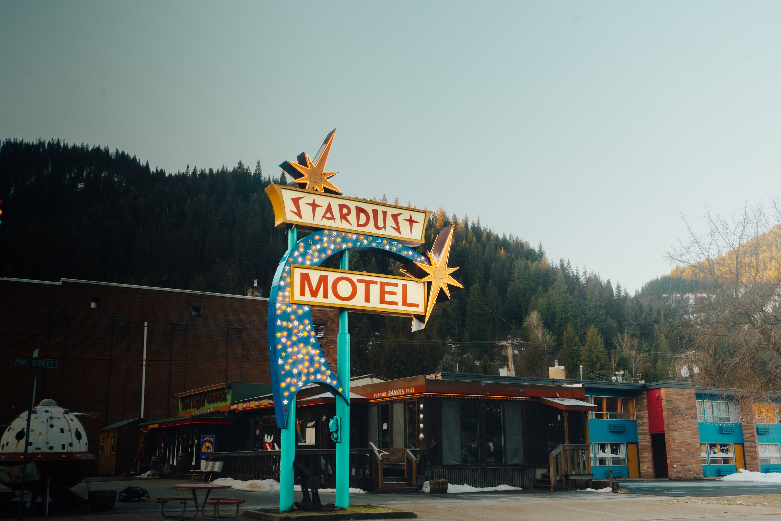 Vintage motel sign and buildings nestled in a forested mountain setting at dusk.