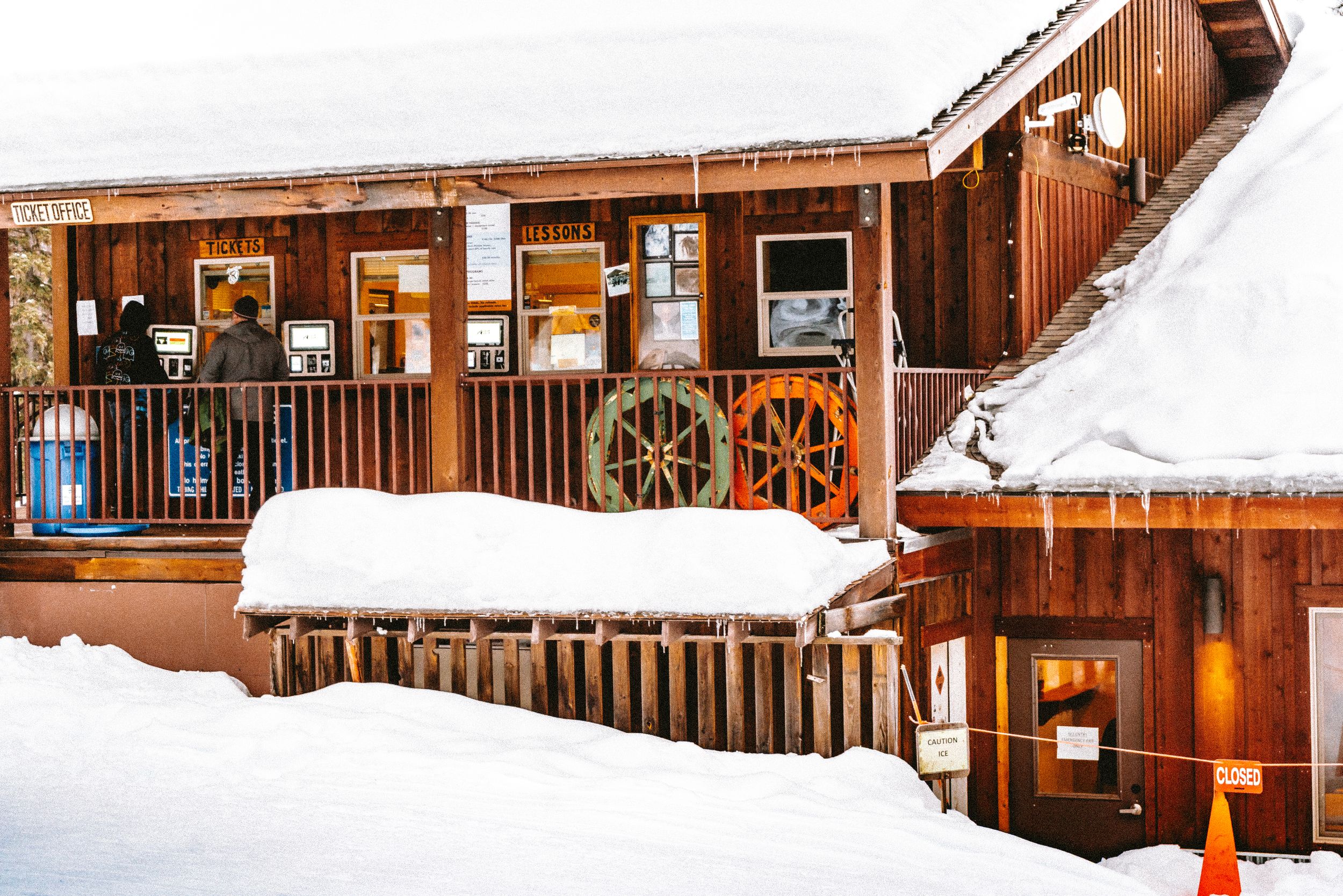 Snow-covered wooden lodge buildings with rustic architecture and warm lighting.