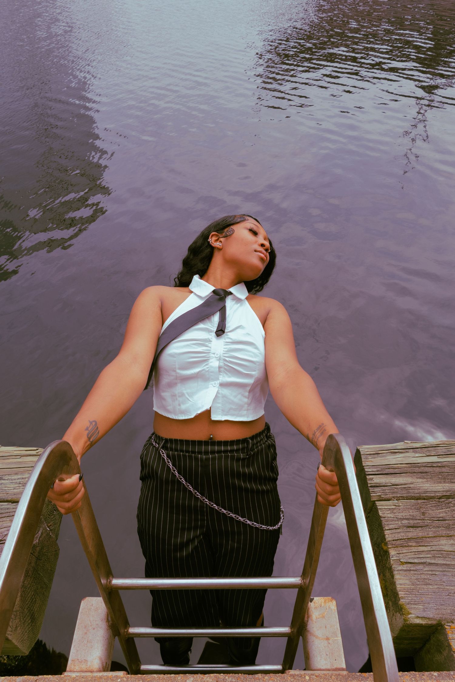 Person relaxing on wooden dock stairs over purple-tinted water on a calm day.
