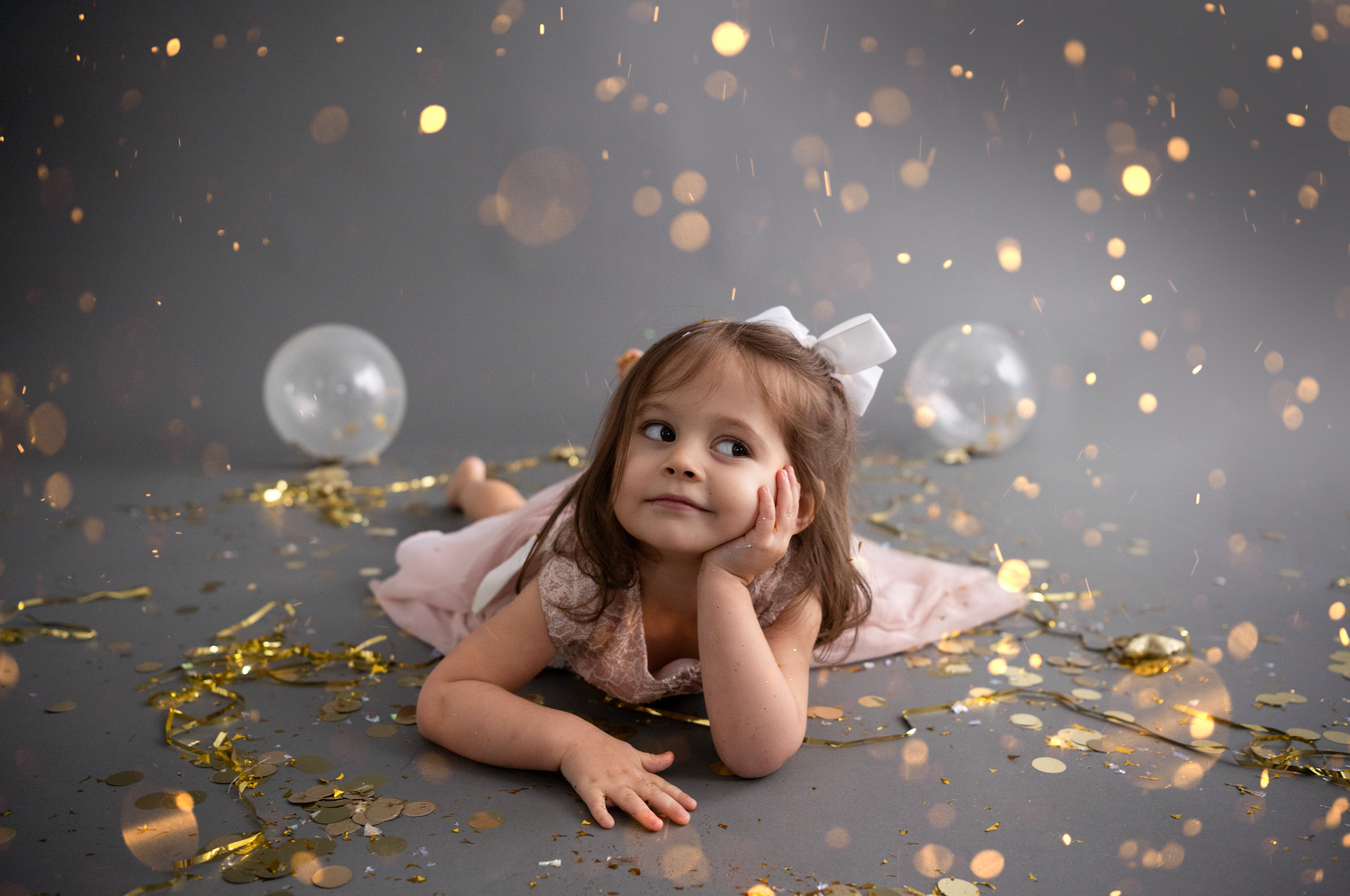 A person lies on the floor surrounded by glittering gold confetti and bokeh lights creating a dreamy atmosphere.