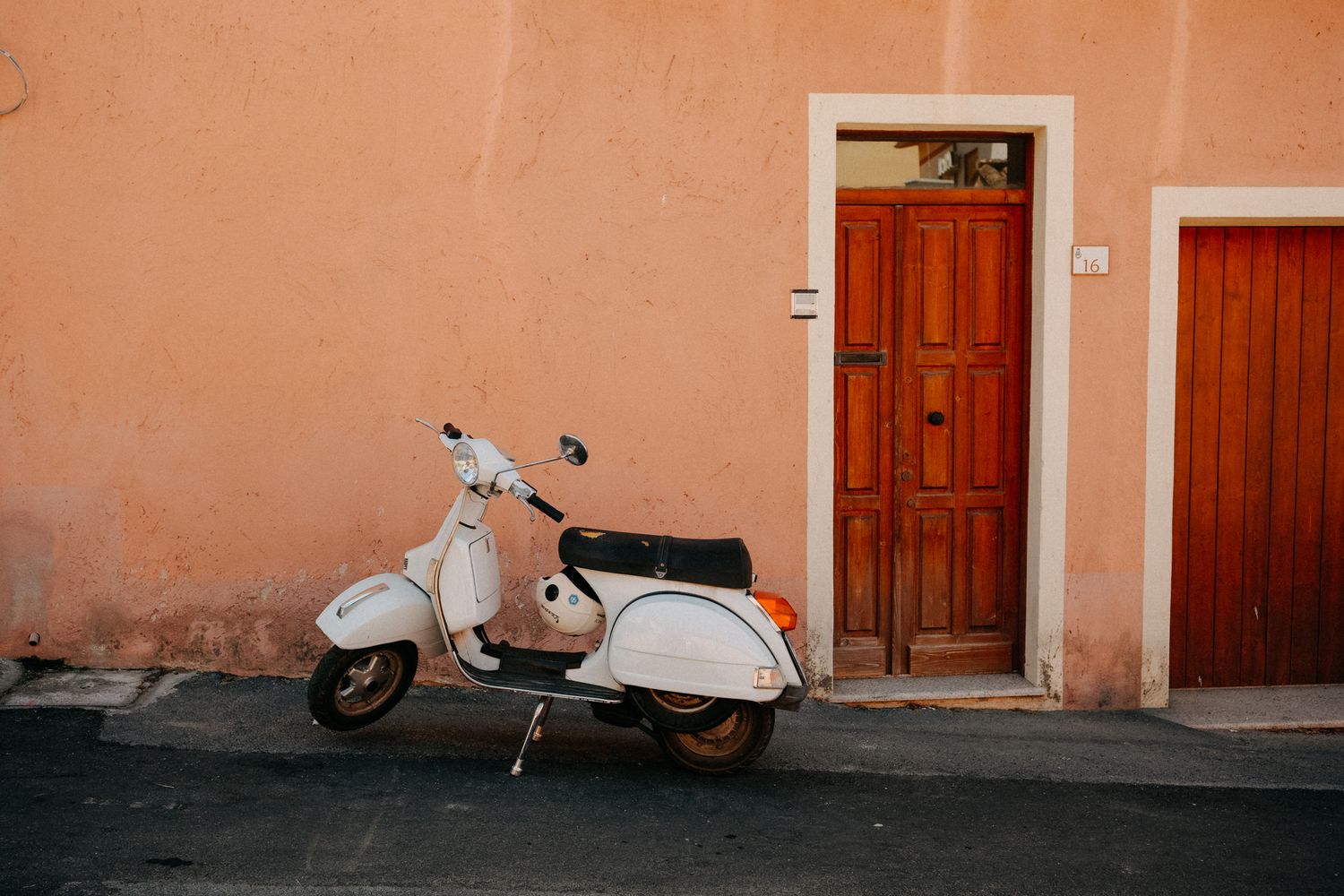 Vintage scooter parked against coral-colored wall with wooden doors.