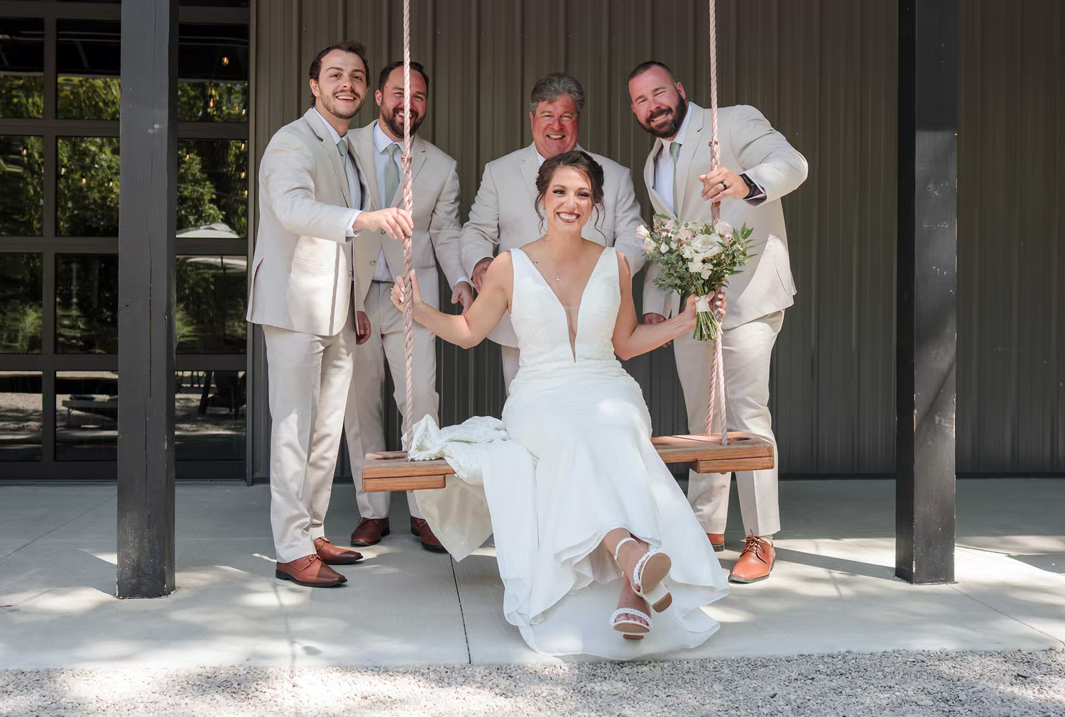 Wedding party in light colored attire poses together on porch swing at Retreat 21 Wedding Venue