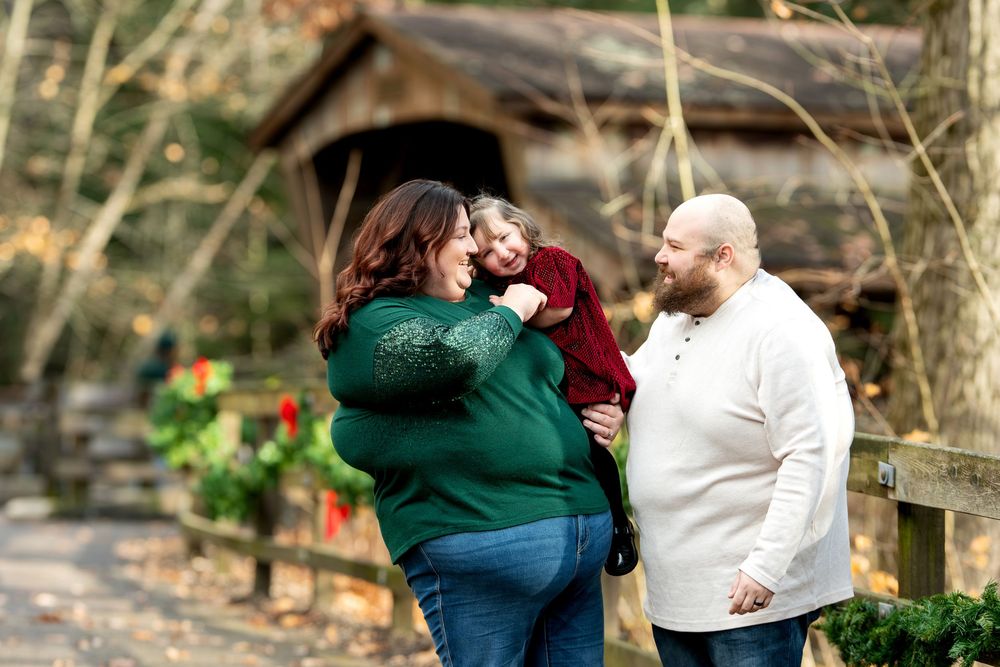 A joyful family moment as a mother holds her laughing toddler while father smiles beside a festive fence.